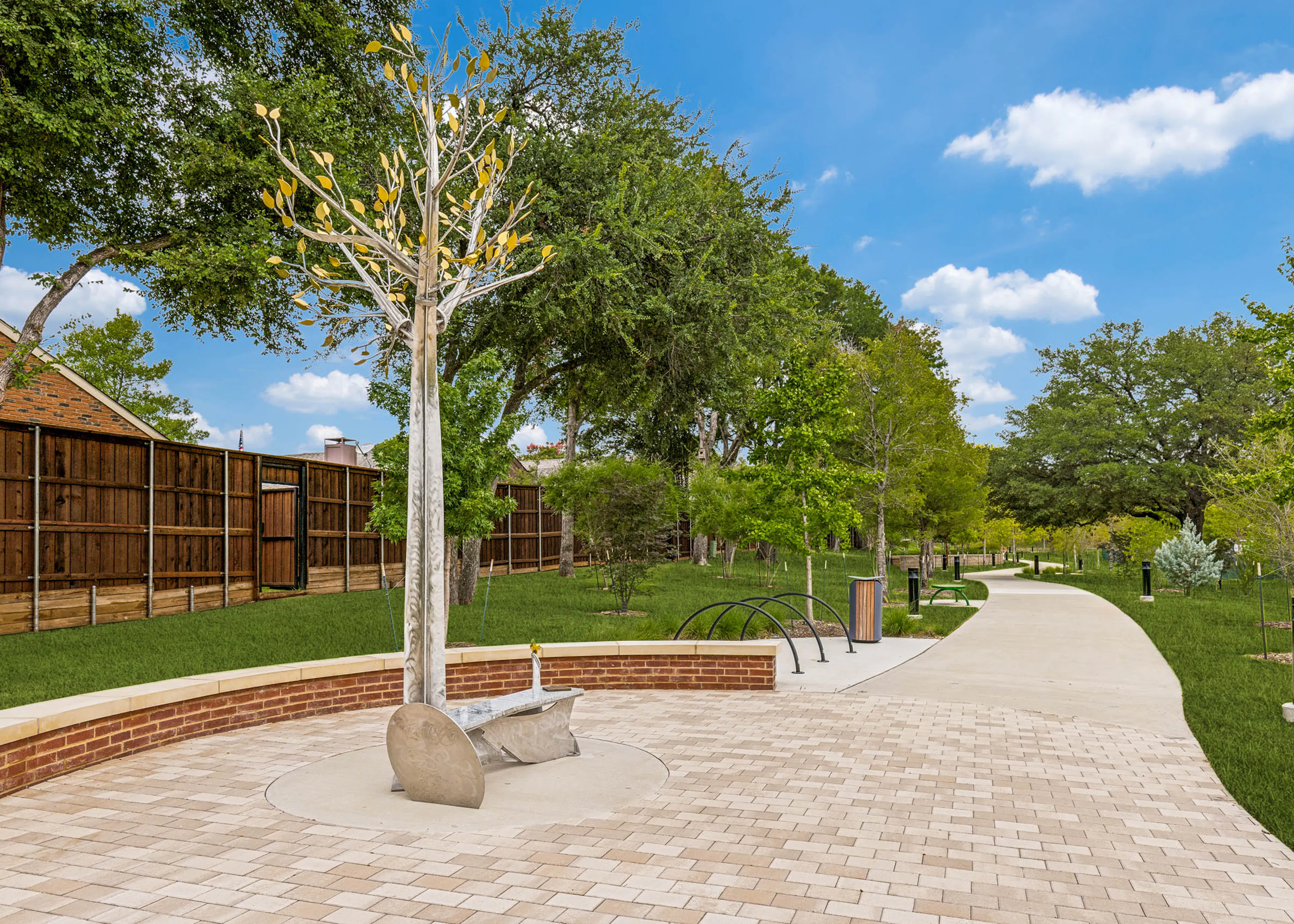Park-like community trail featuring a decorative tree sculpture, paved seating area, landscaped greenery, pathway lighting, and open green space at AMLI Treehouse.