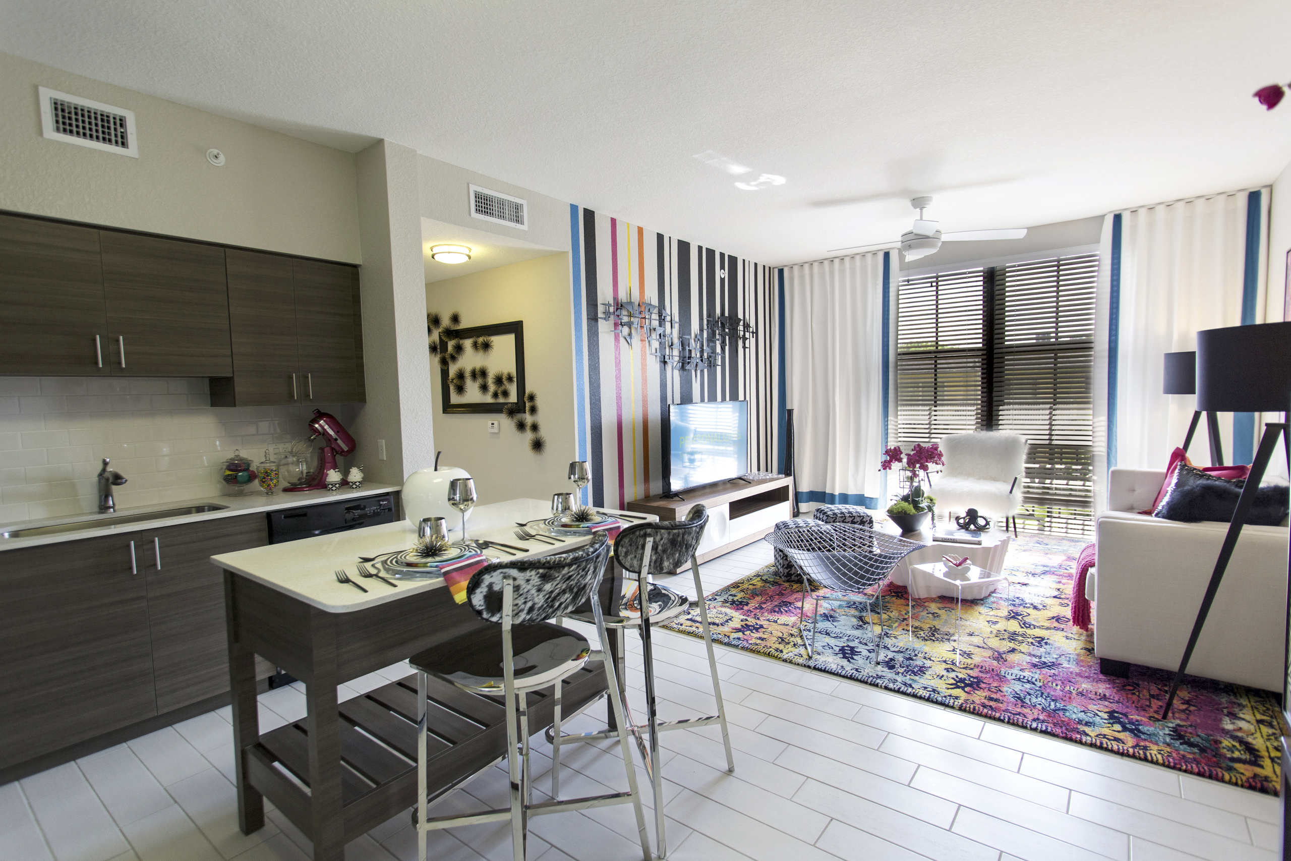 AMLI Dadeland apartment living area with black and white wall, TV on console, hounds tooth stools and a peek into the kitchen