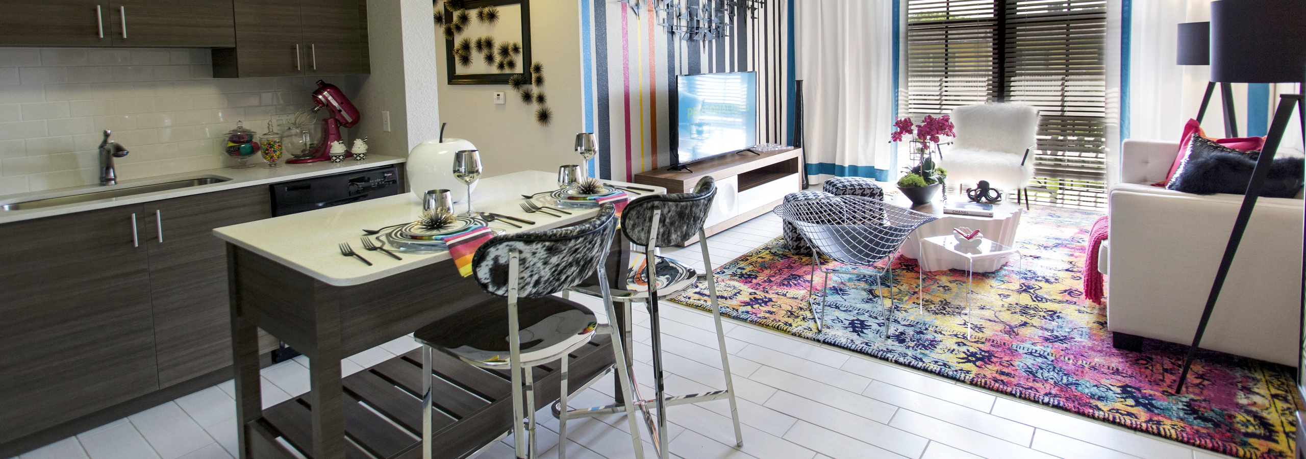 AMLI Dadeland apartment living area with black and white wall, TV on console, hounds tooth stools and a peek into the kitchen