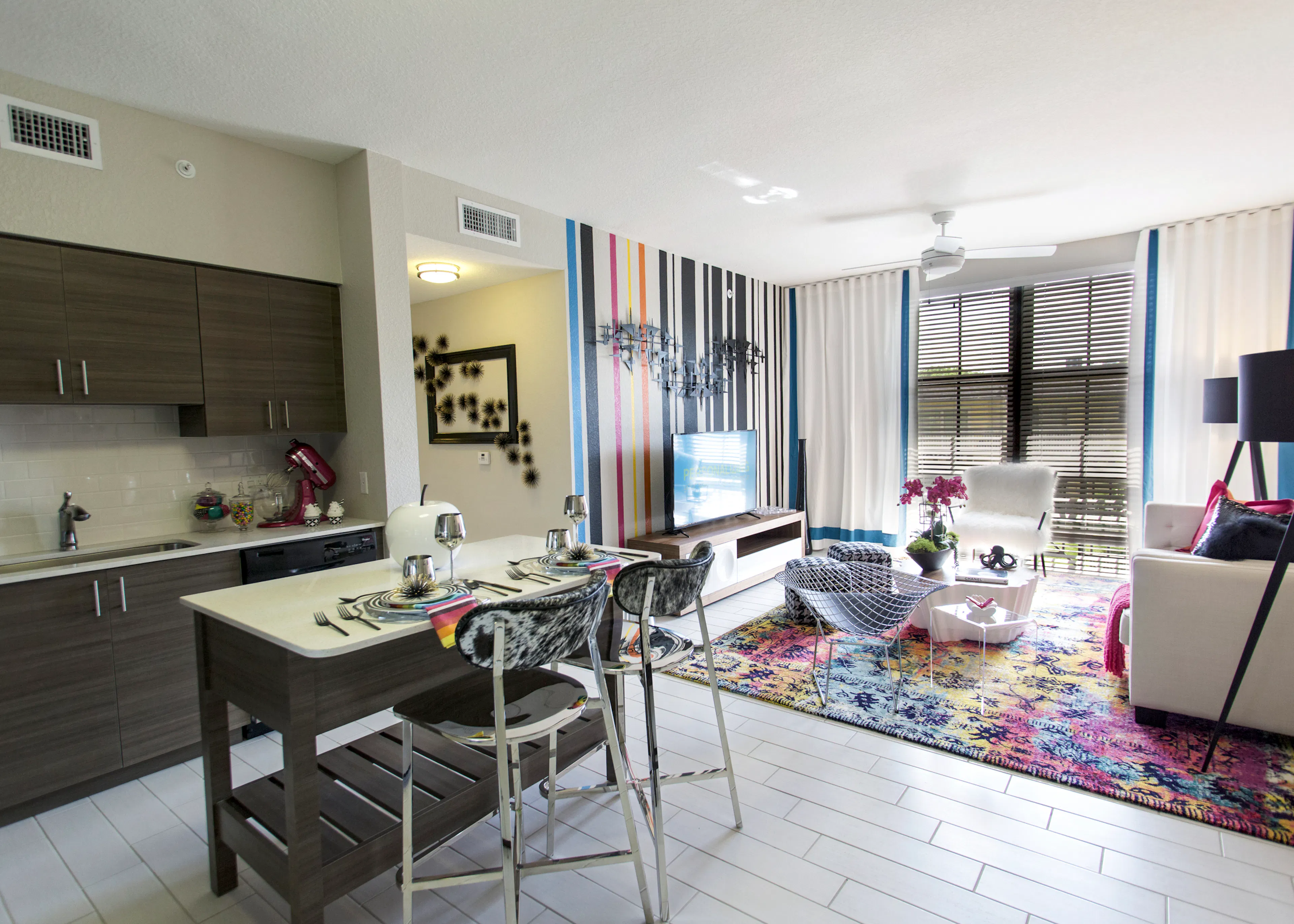 AMLI Dadeland apartment living area with black and white wall, TV on console, hounds tooth stools and a peek into the kitchen