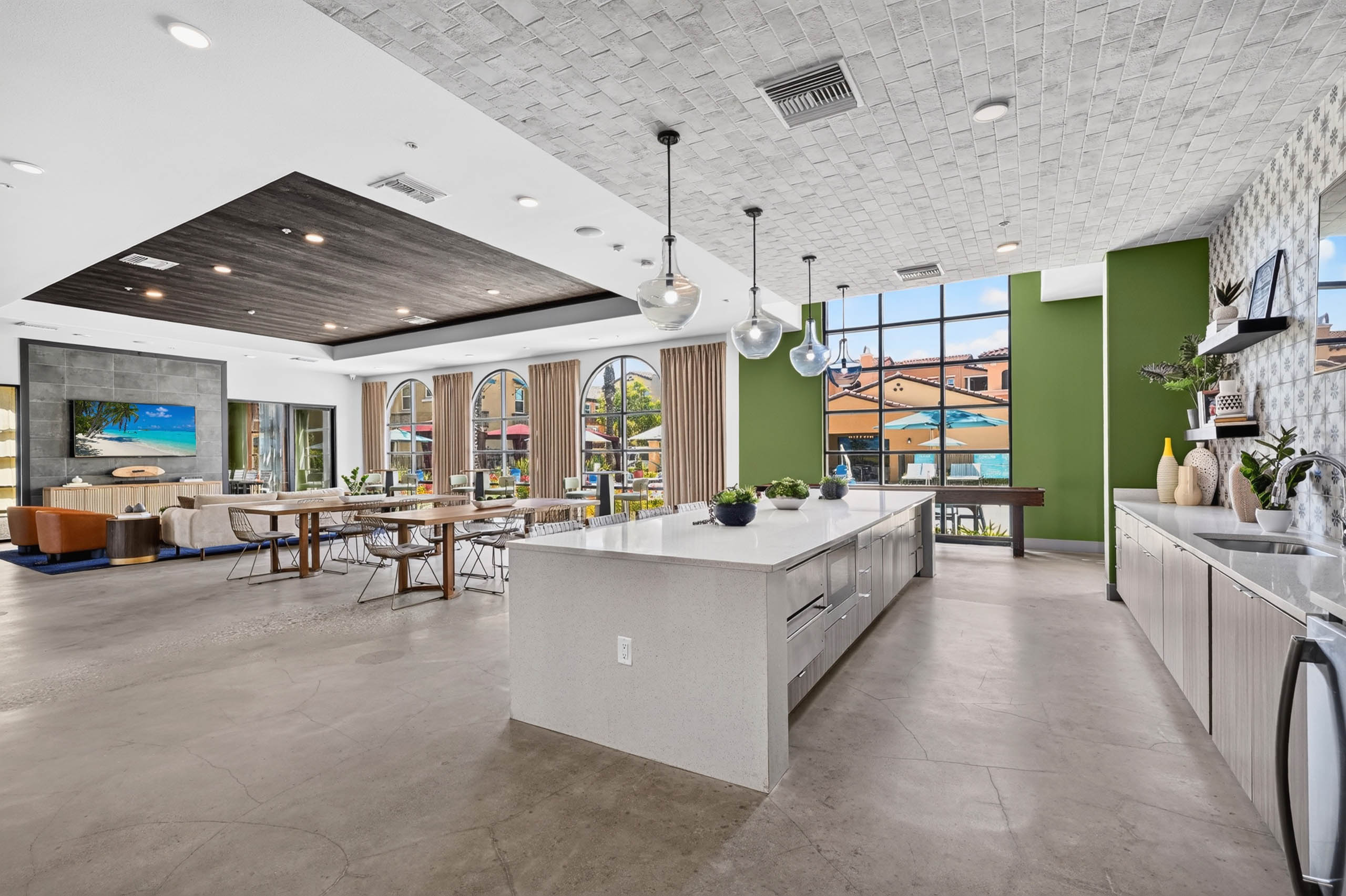 Wide view of AMLI Camarillo apartments clubhouse with kitchen island, dining tables, lounge seating and large courtyard windows