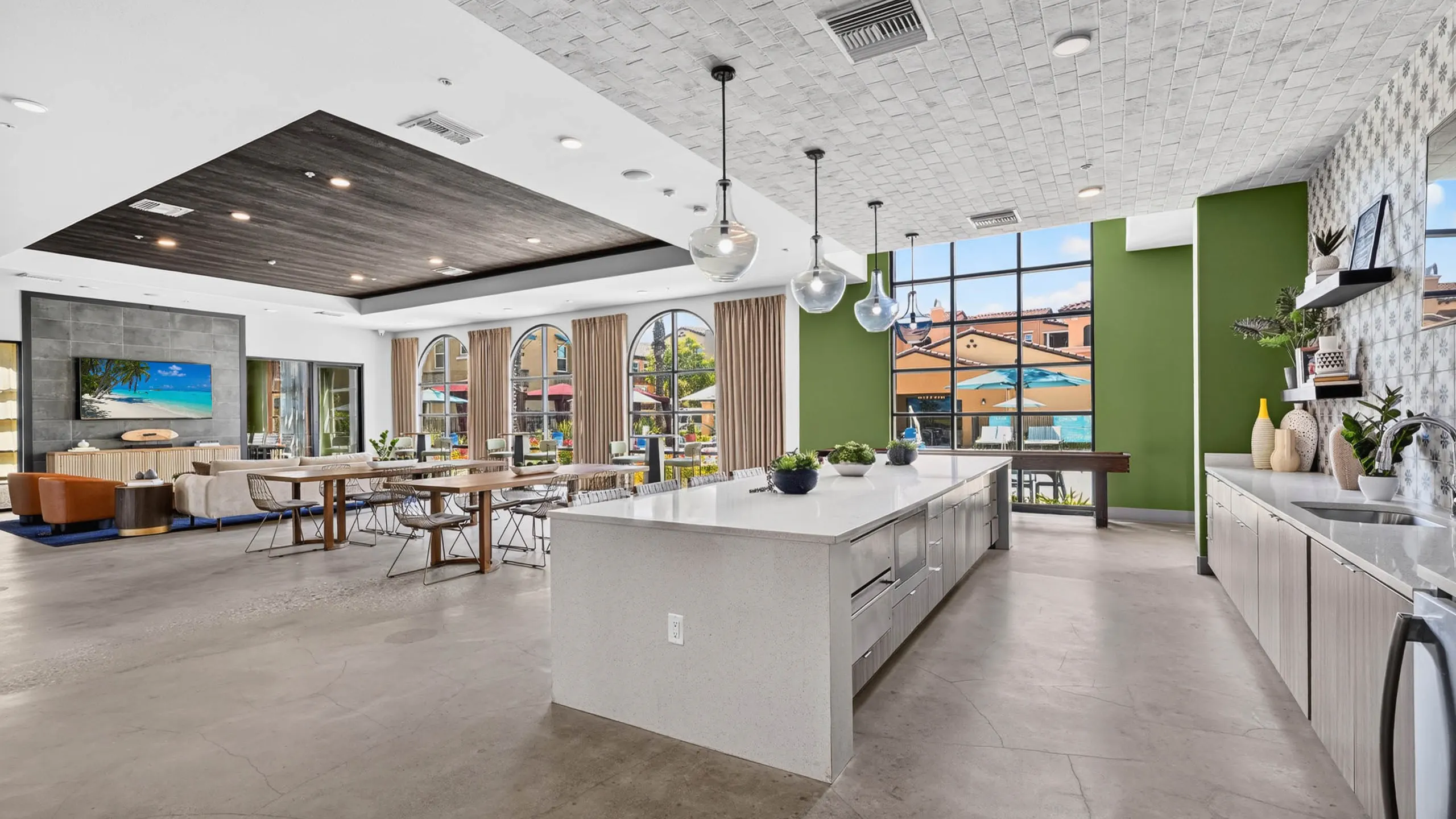 Wide view of AMLI Camarillo apartments clubhouse with kitchen island, dining tables, lounge seating and large courtyard windows