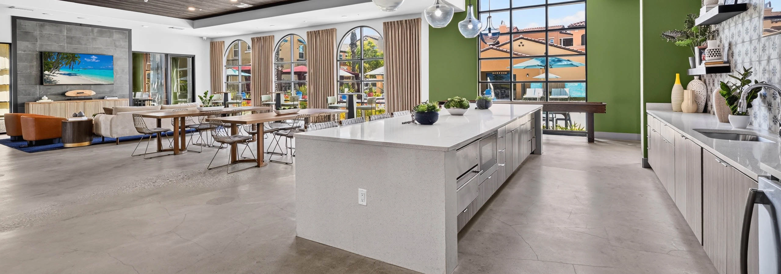 Wide view of AMLI Camarillo apartments clubhouse with kitchen island, dining tables, lounge seating and large courtyard windows
