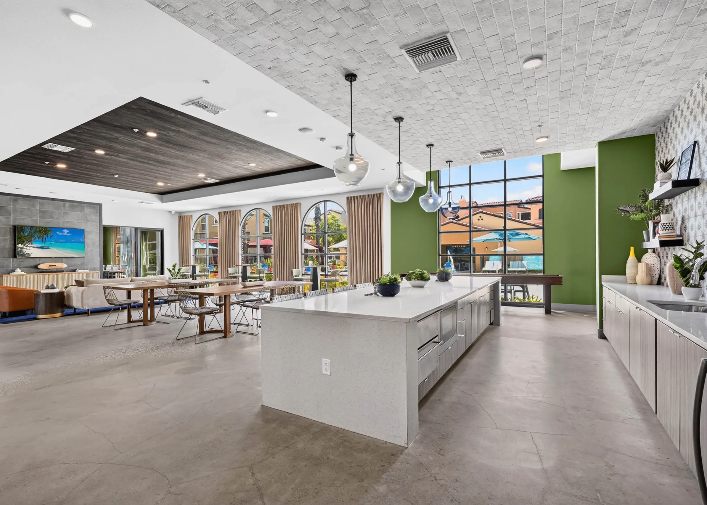 Wide view of AMLI Camarillo apartments clubhouse with kitchen island, dining tables, lounge seating and large courtyard windows