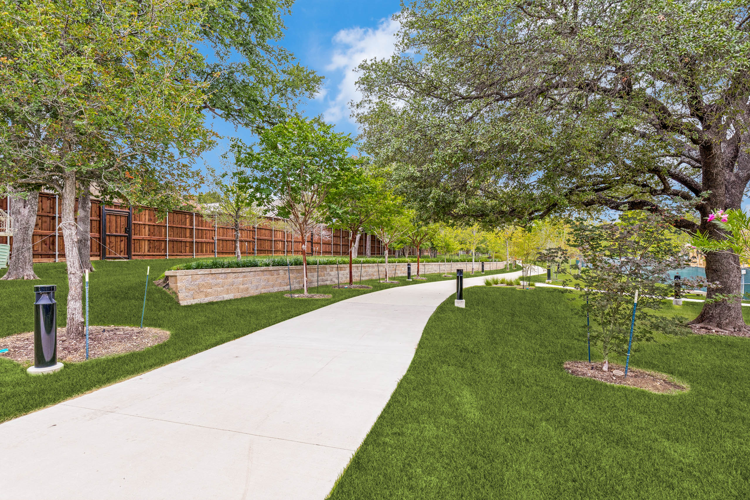 Landscaped walking trail with shaded green space, manicured lawn, retaining wall, pathway lighting, and lush greenery at AMLI Treehouse.