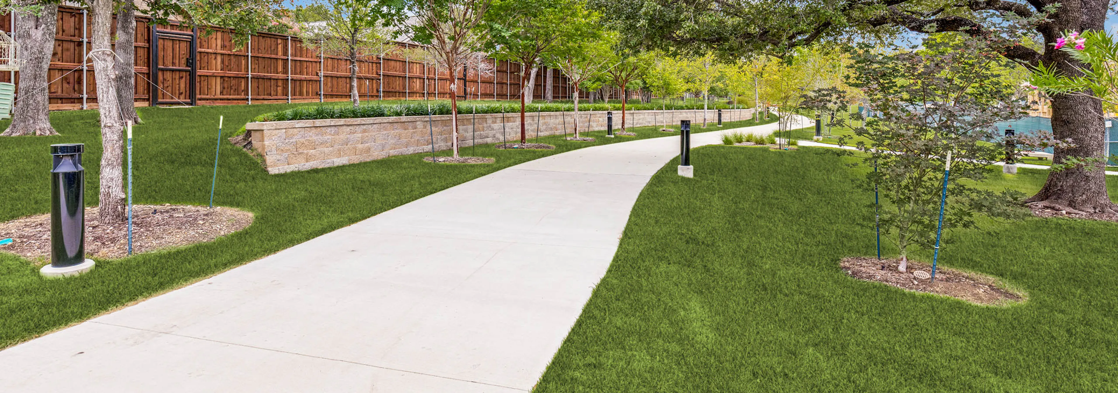 Landscaped walking trail with shaded green space, manicured lawn, retaining wall, pathway lighting, and lush greenery at AMLI Treehouse.
