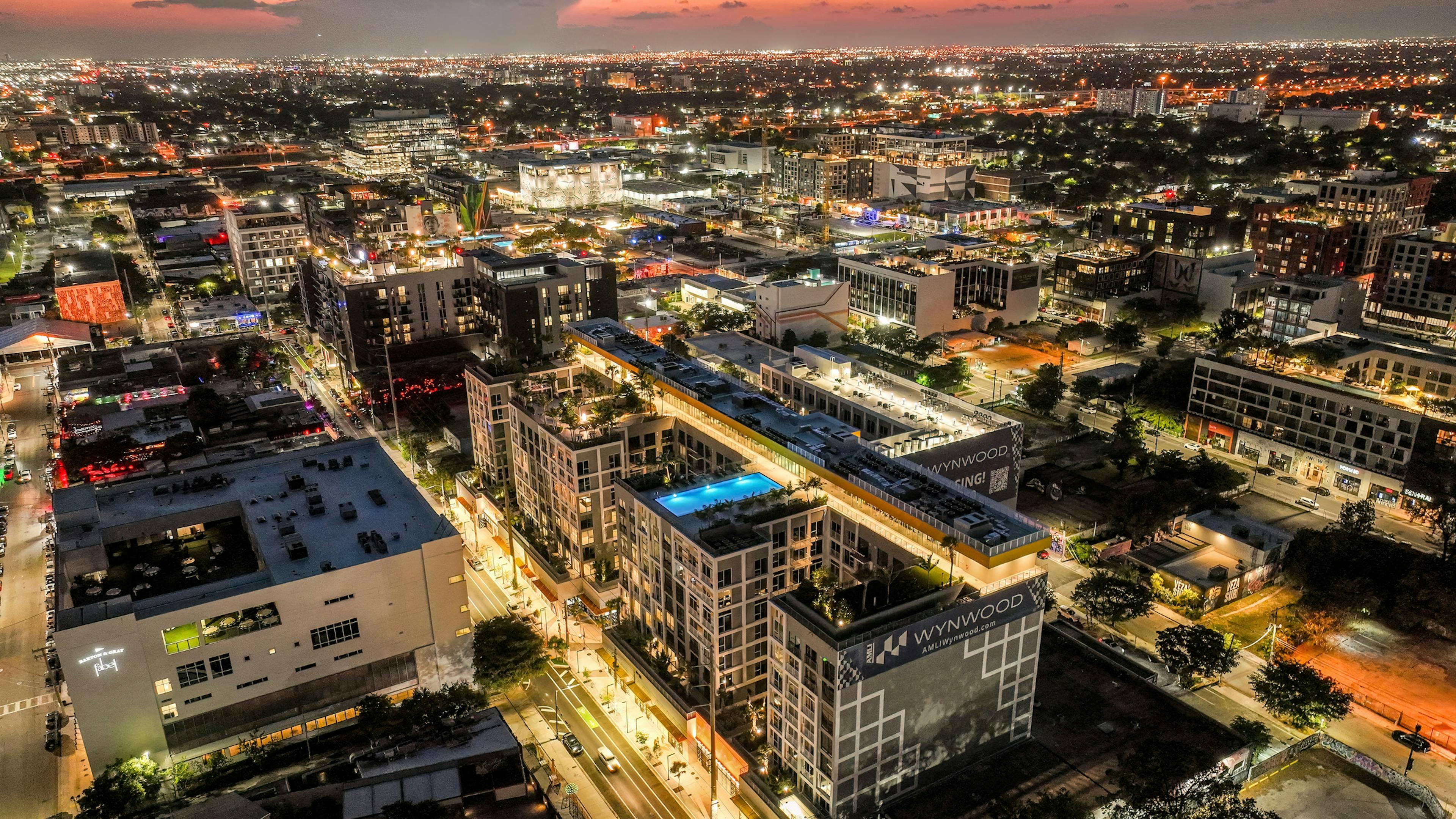 Nighttime aerial view of AMLI Wynwood with roof deck amenities and a swimming pool featured and city skyline