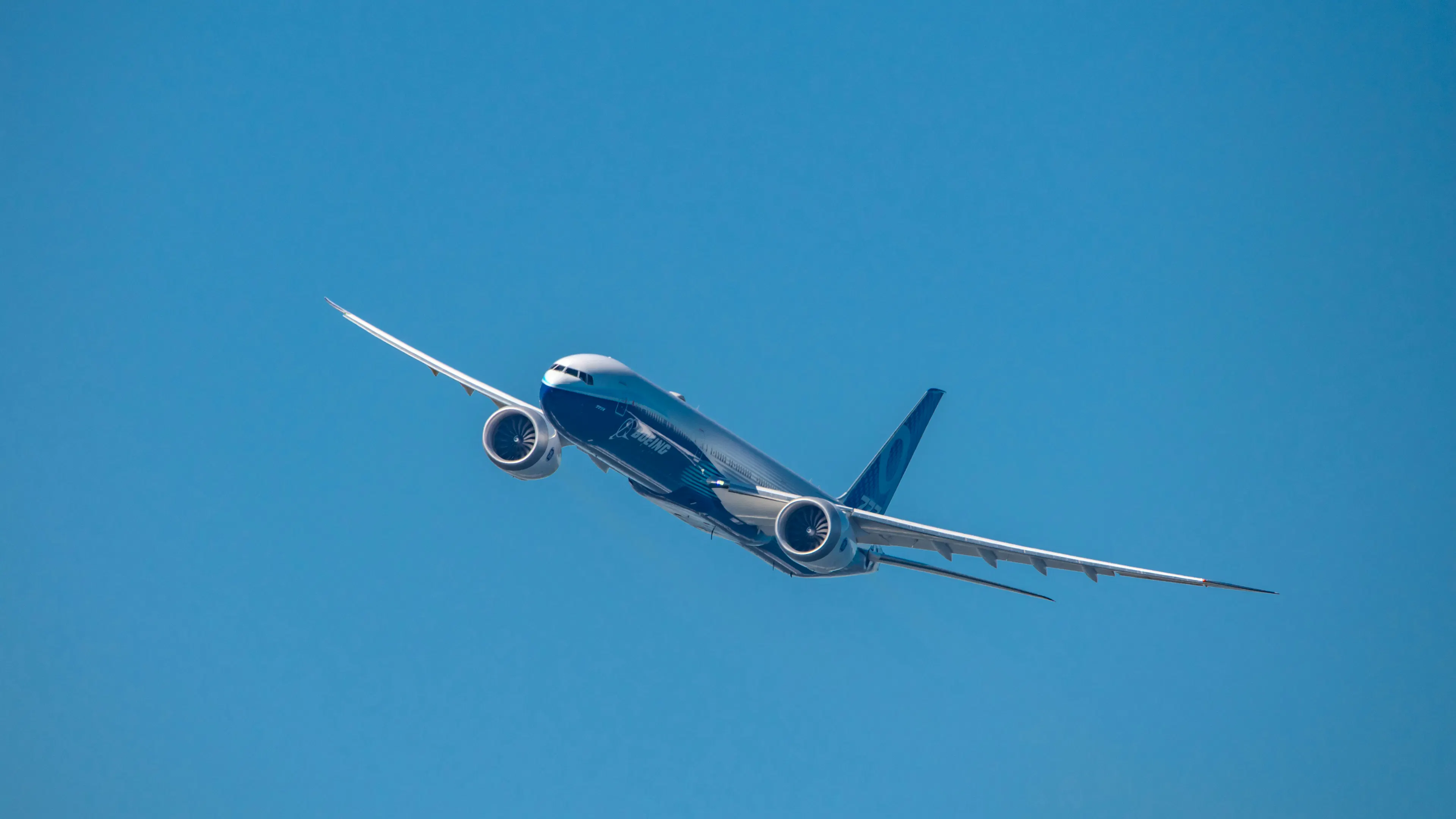 A Boeing 777X flying toward the viewer on a clear blue day