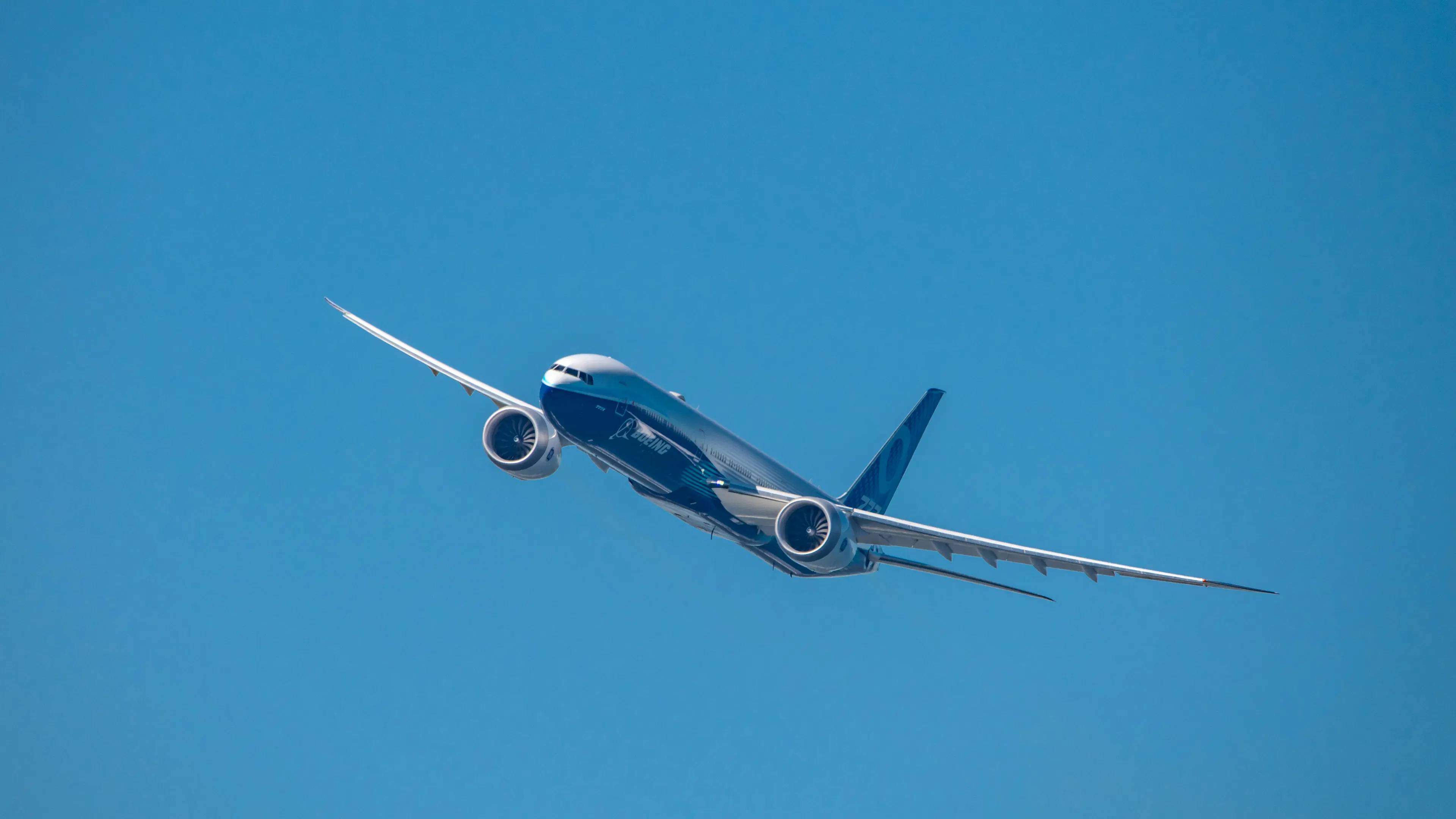 A Boeing 777X flying toward the viewer on a clear blue day