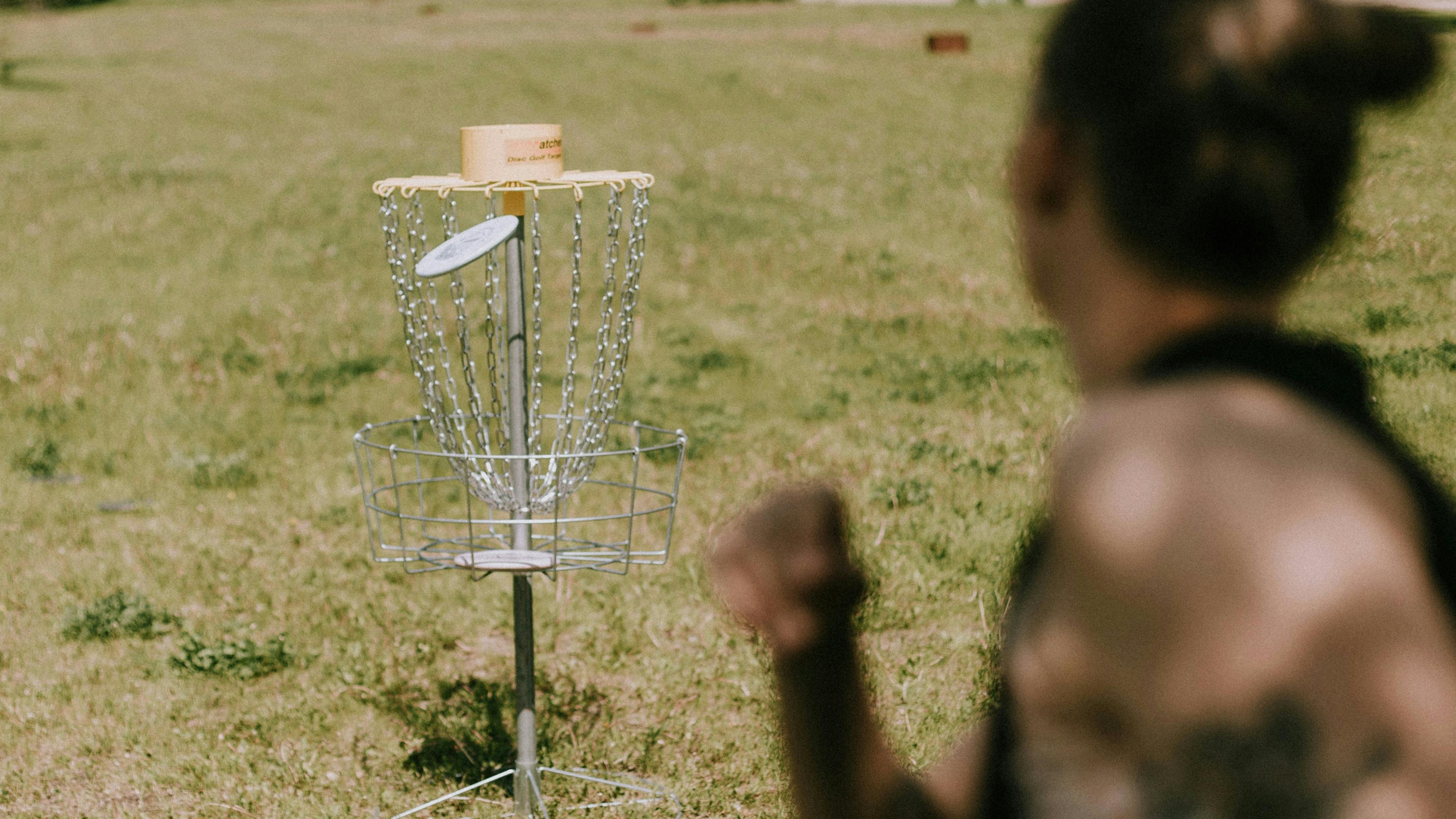 A woman throwing a frisbee golf disc into a disc golf net on a grassy field