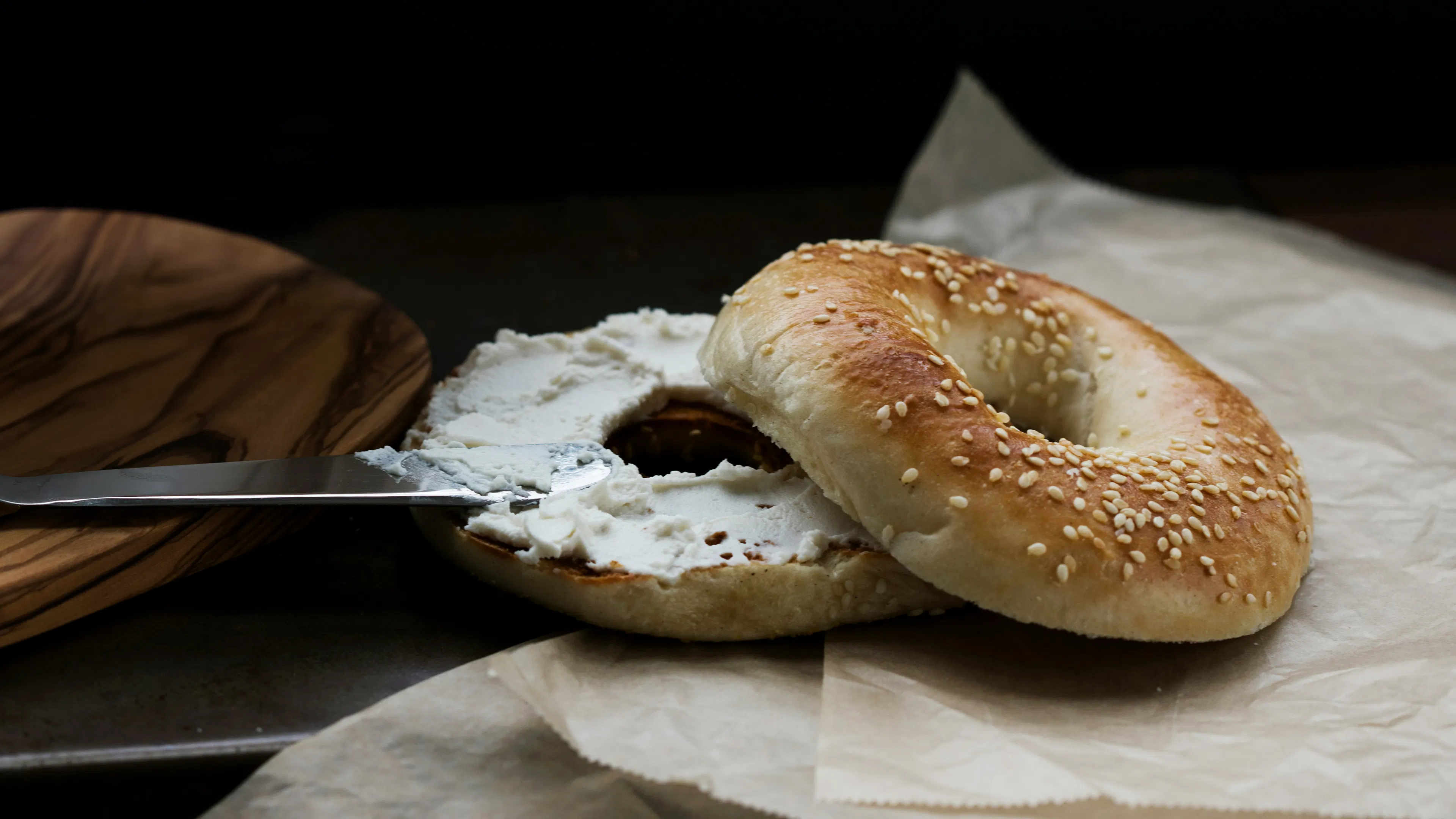 A sliced sesame bagel with cream cheese spread on it