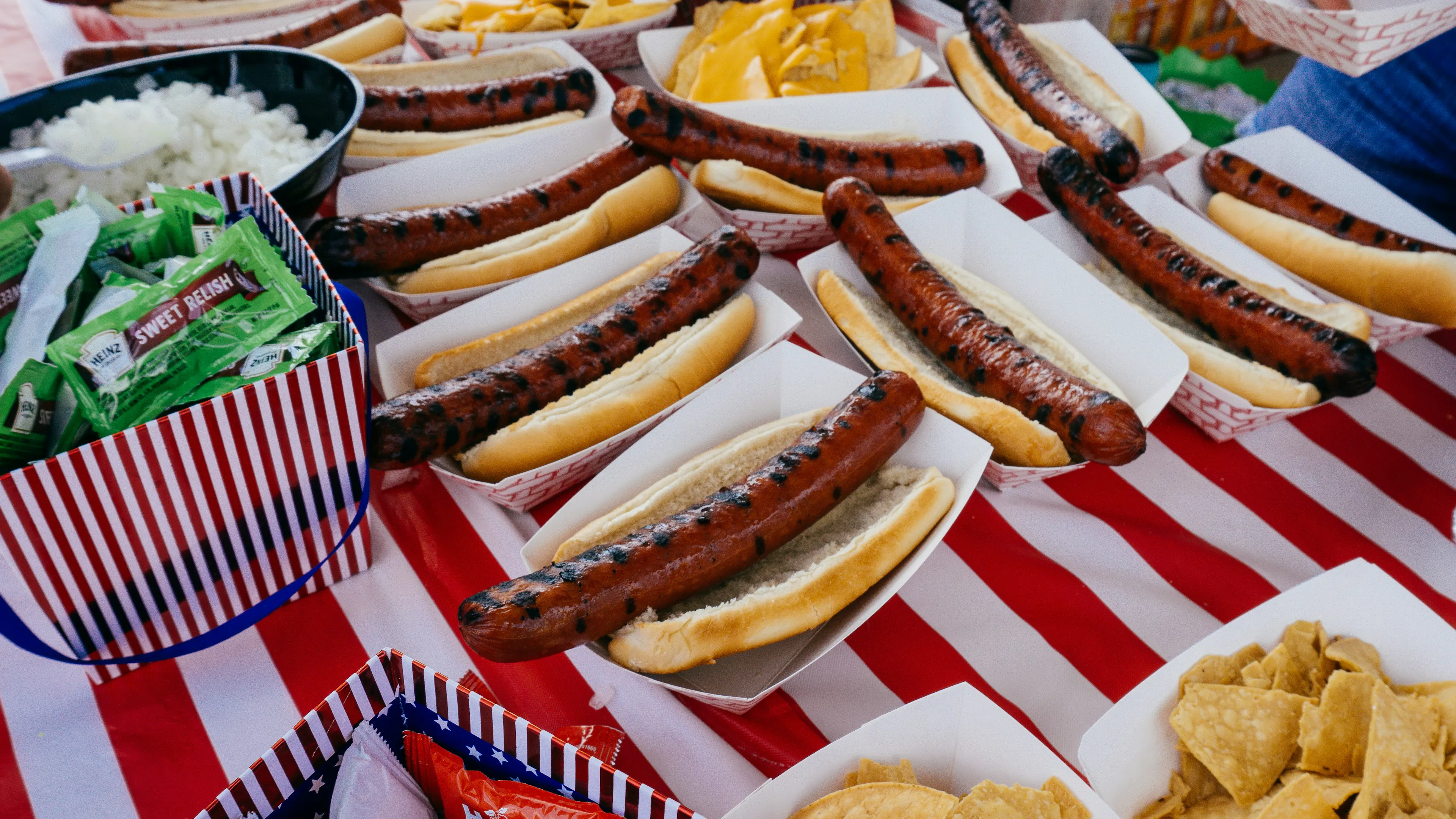 A picnic table with many hot dog containers holding foot long hot dogs