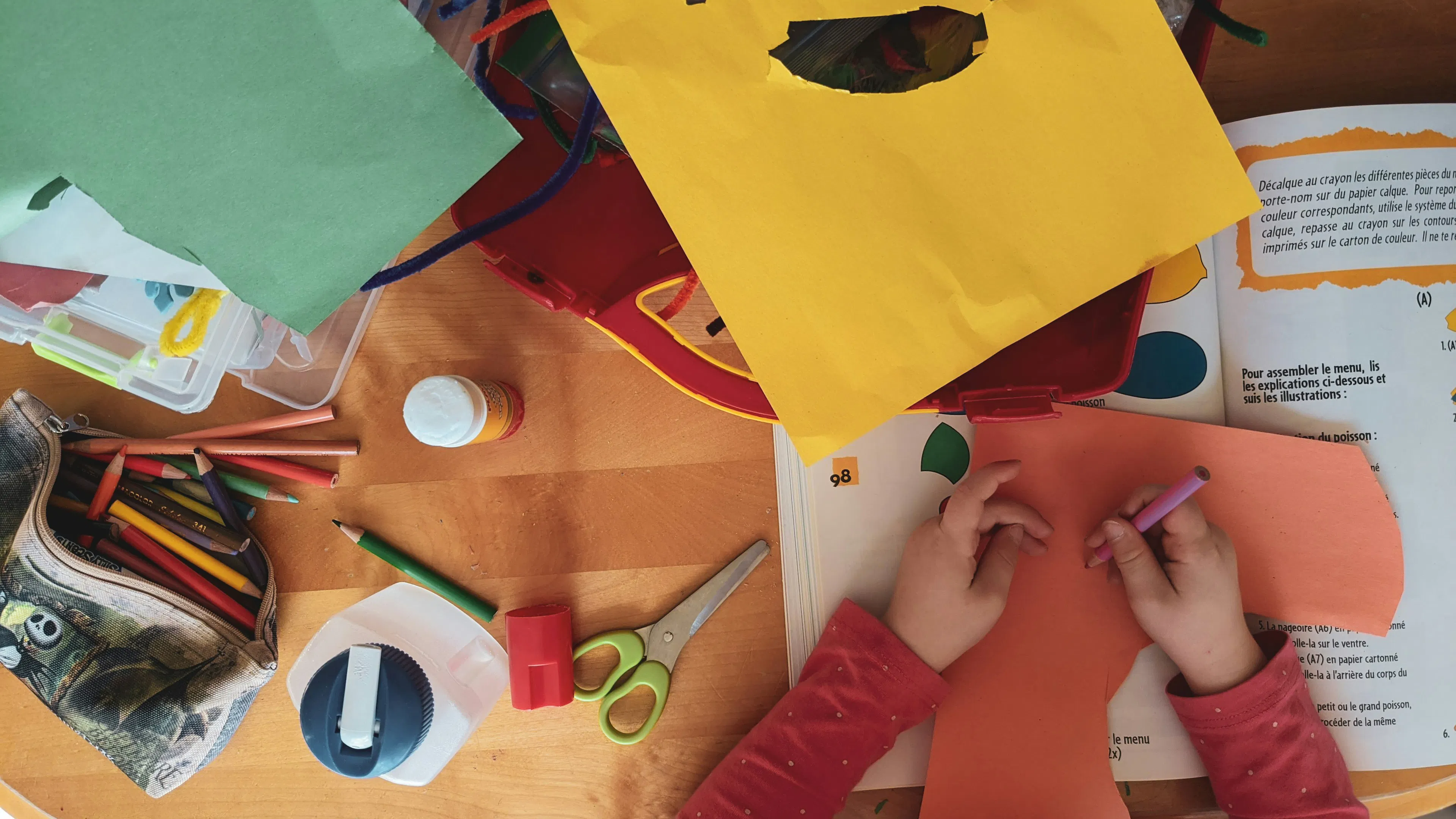 an overhead photo of kids cutting out shapes from brightly colored paper