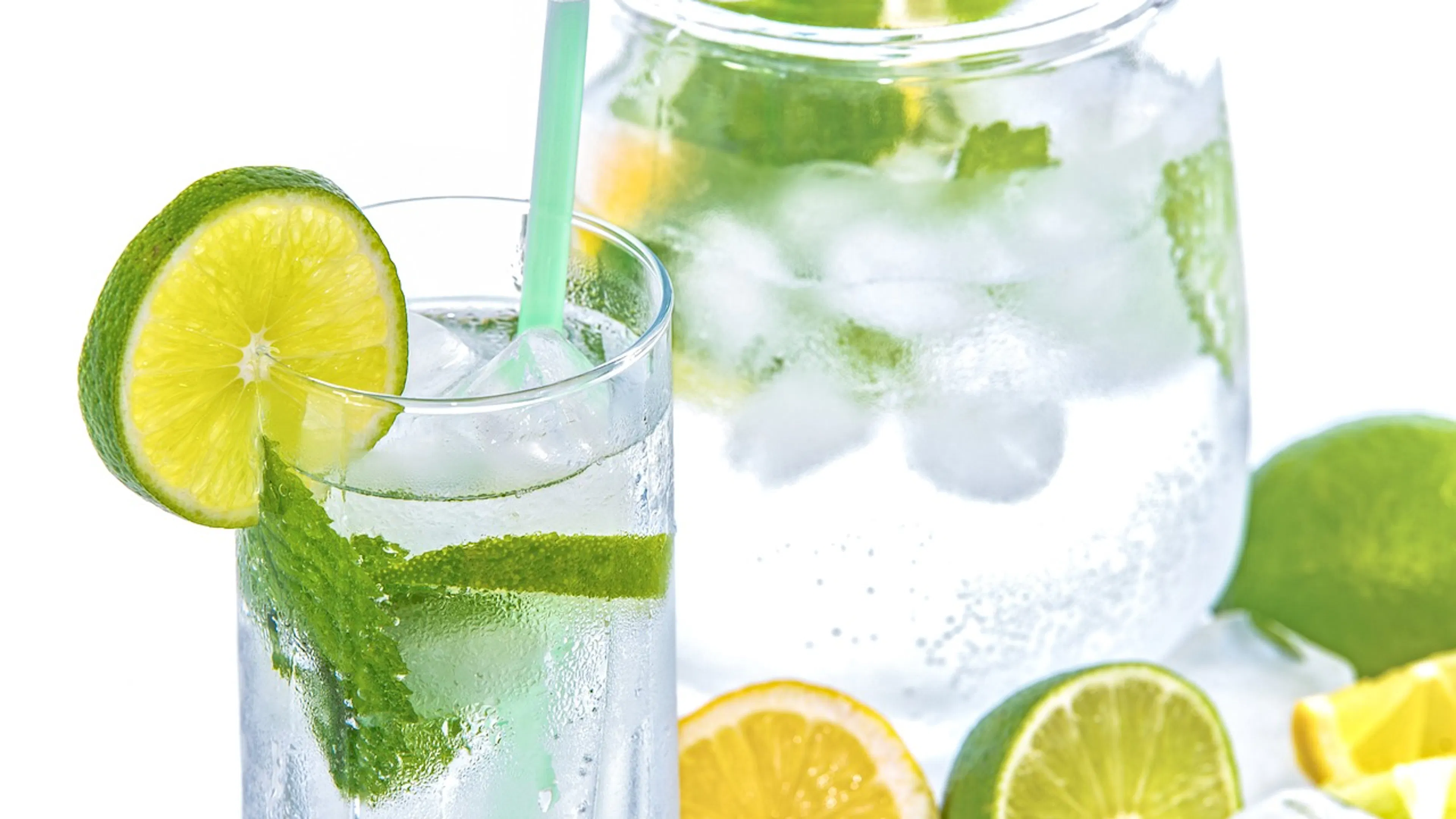 Glass pitcher and glass filled with water and cut lemons and limes on a white background