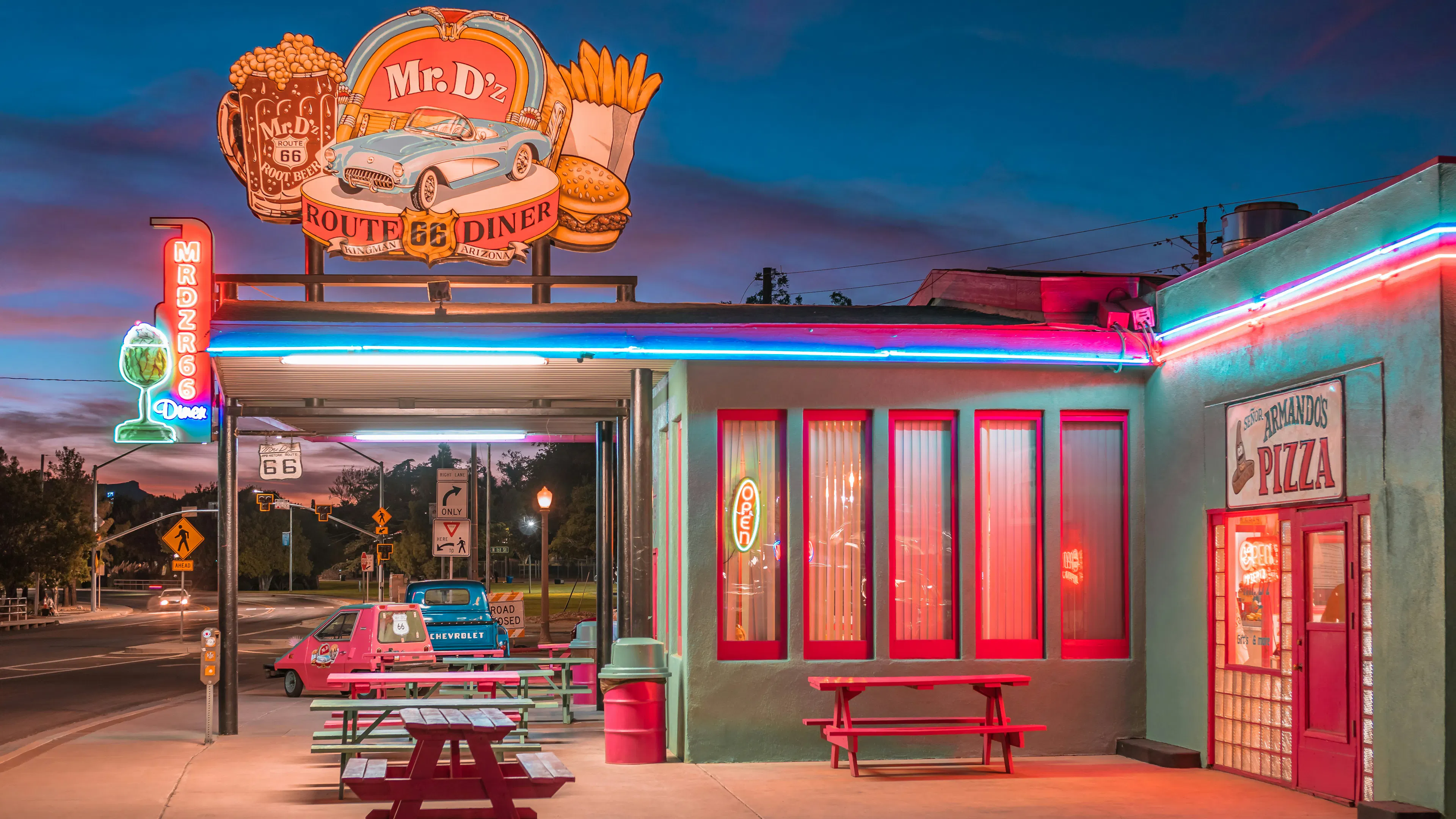 The exterior of a Route 66 diner with red lights and neon lights shining in the twilight