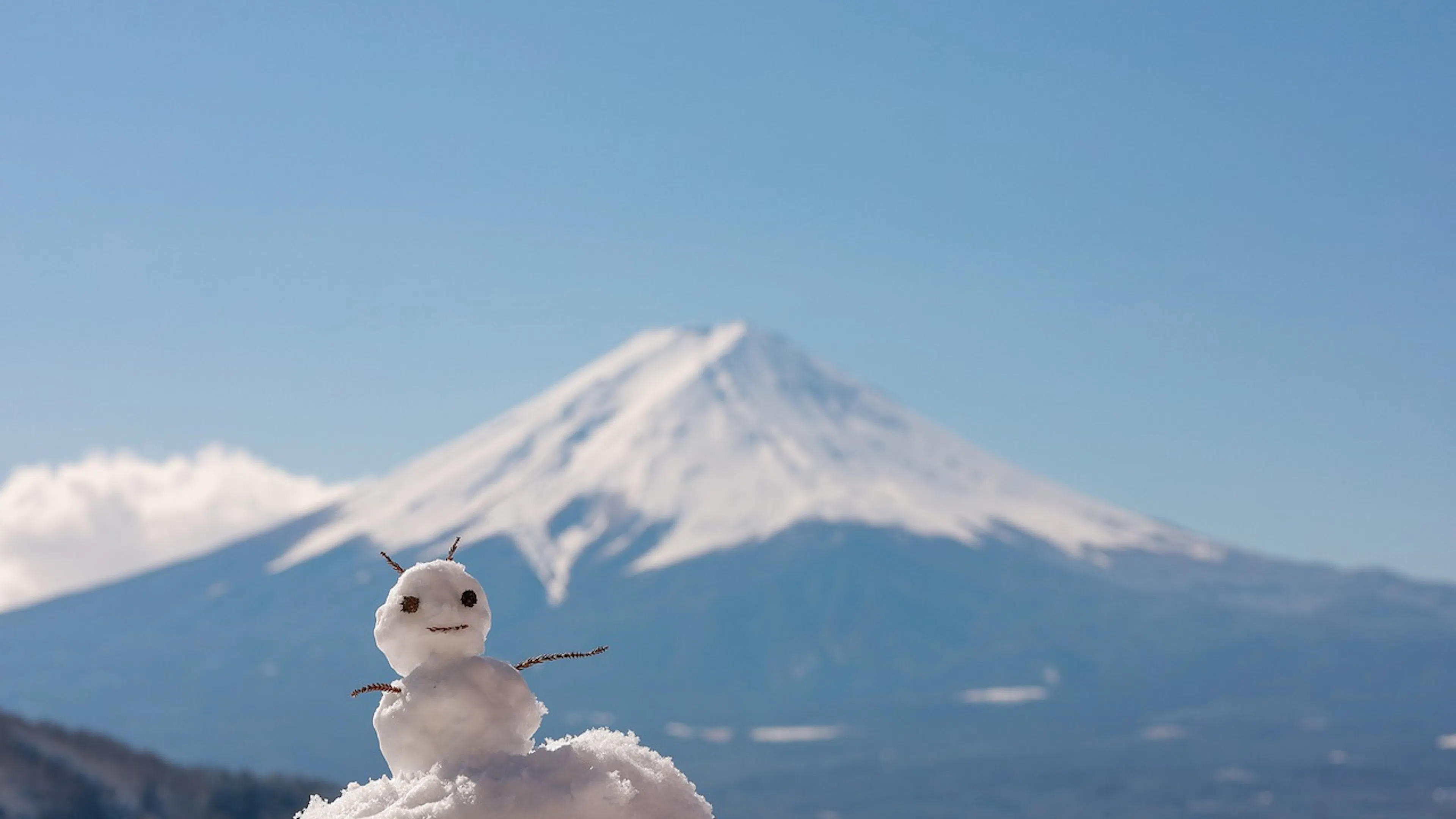 small snowman in front of large mountain topped with snow on a blue background
