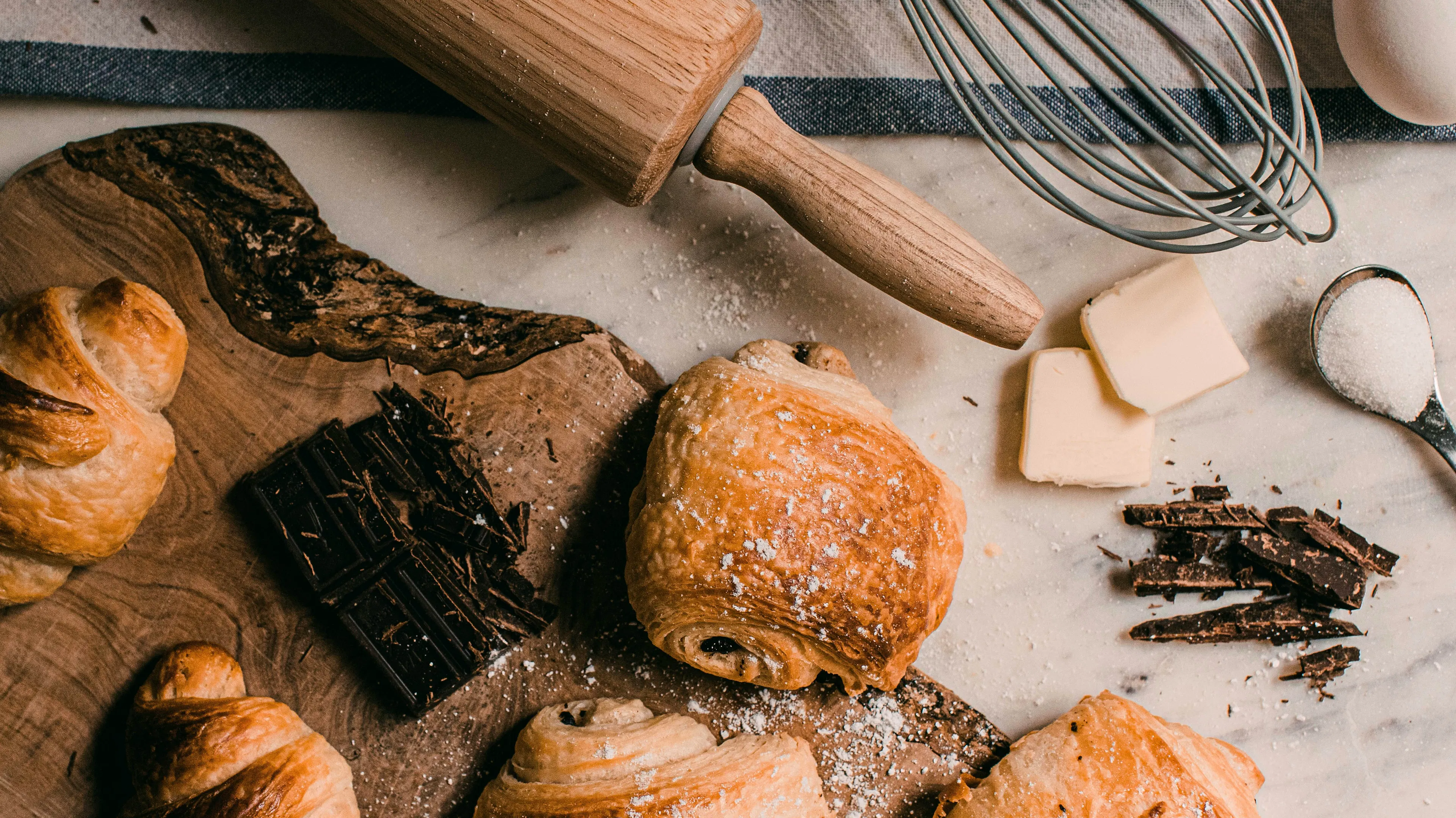 a brown wooden rolling pin beside a whisk and some baked pastries