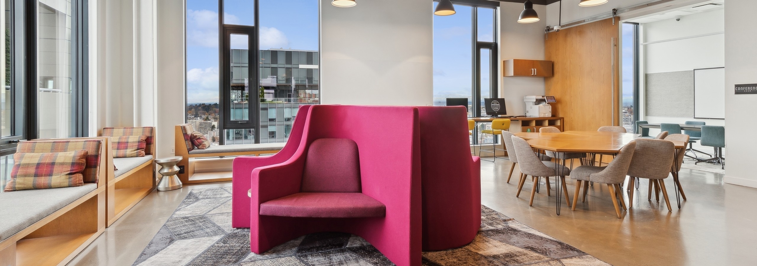Collaboration space at AMLI Arc with bold pink seating, cozy tables and large windows offering natural light and urban views