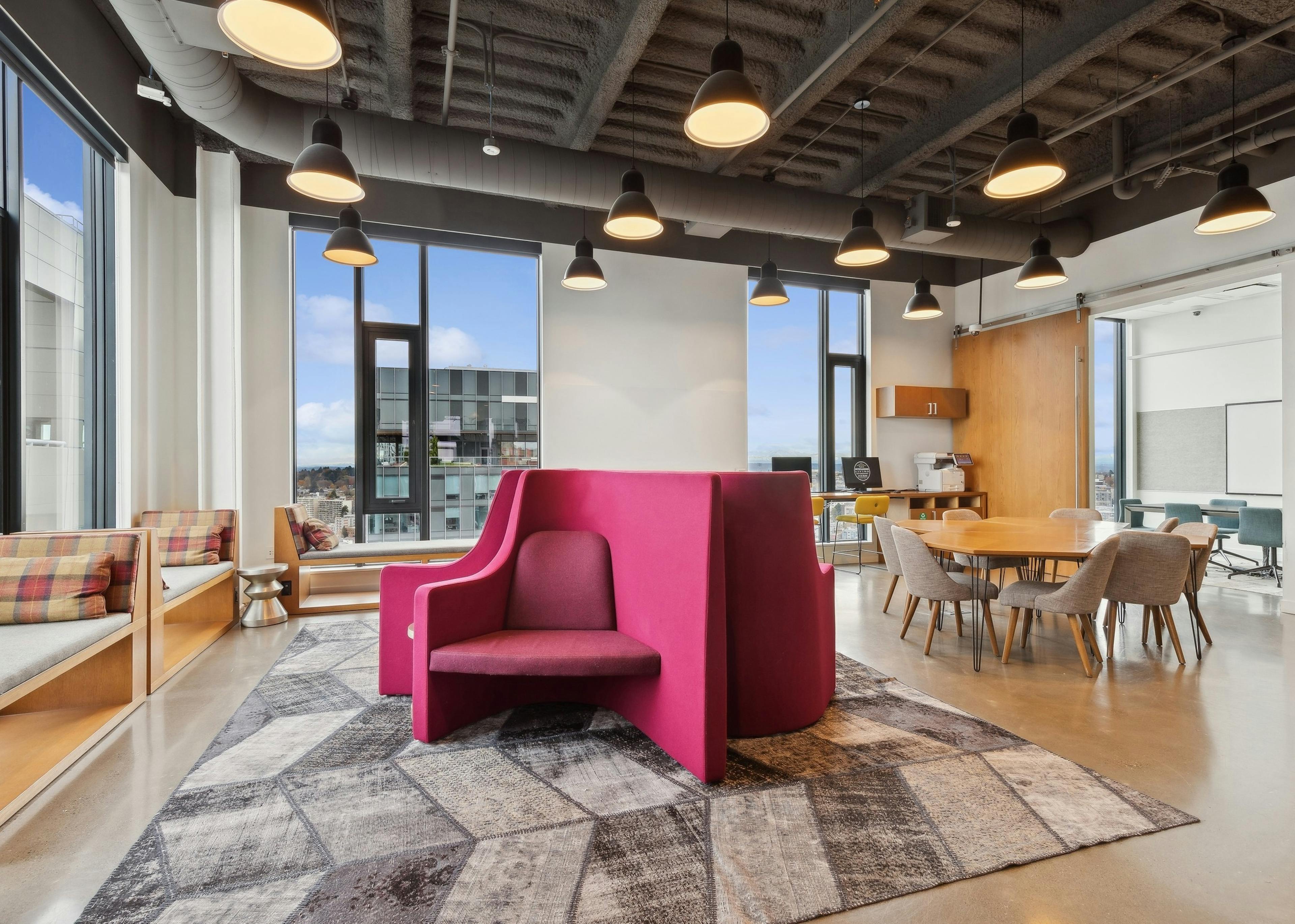 Collaboration space at AMLI Arc with bold pink seating, cozy tables and large windows offering natural light and urban views
