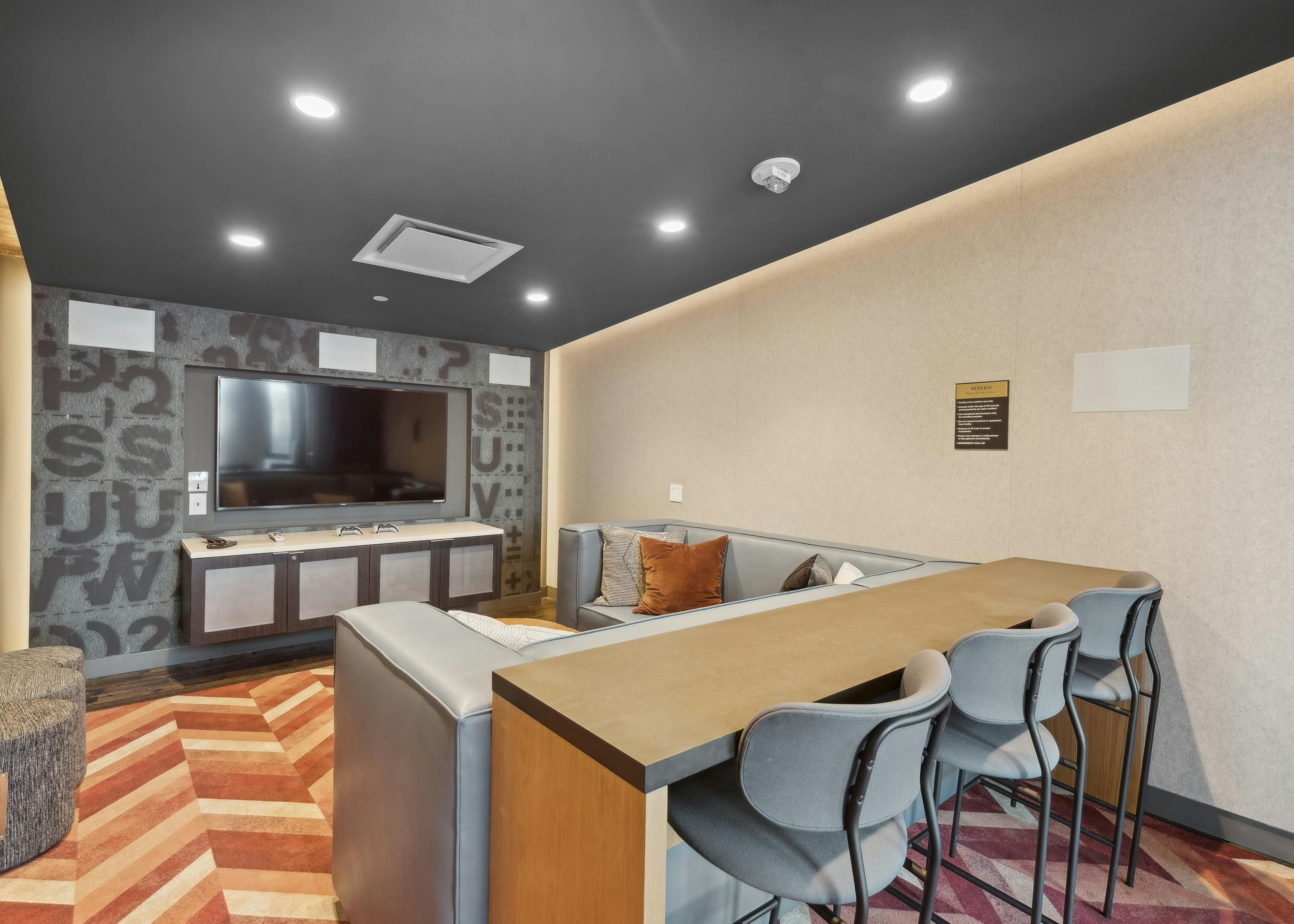 Media room at AMLI Arc with a large flat-screen TV, plush sectional seating, barstools at a hightop counter