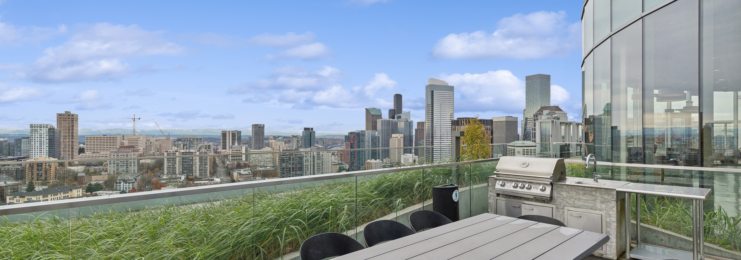 Outdoor terrace with a dining table, grill station, lush landscaping, and sweeping views of the city skyline at AMLI Arc apartments