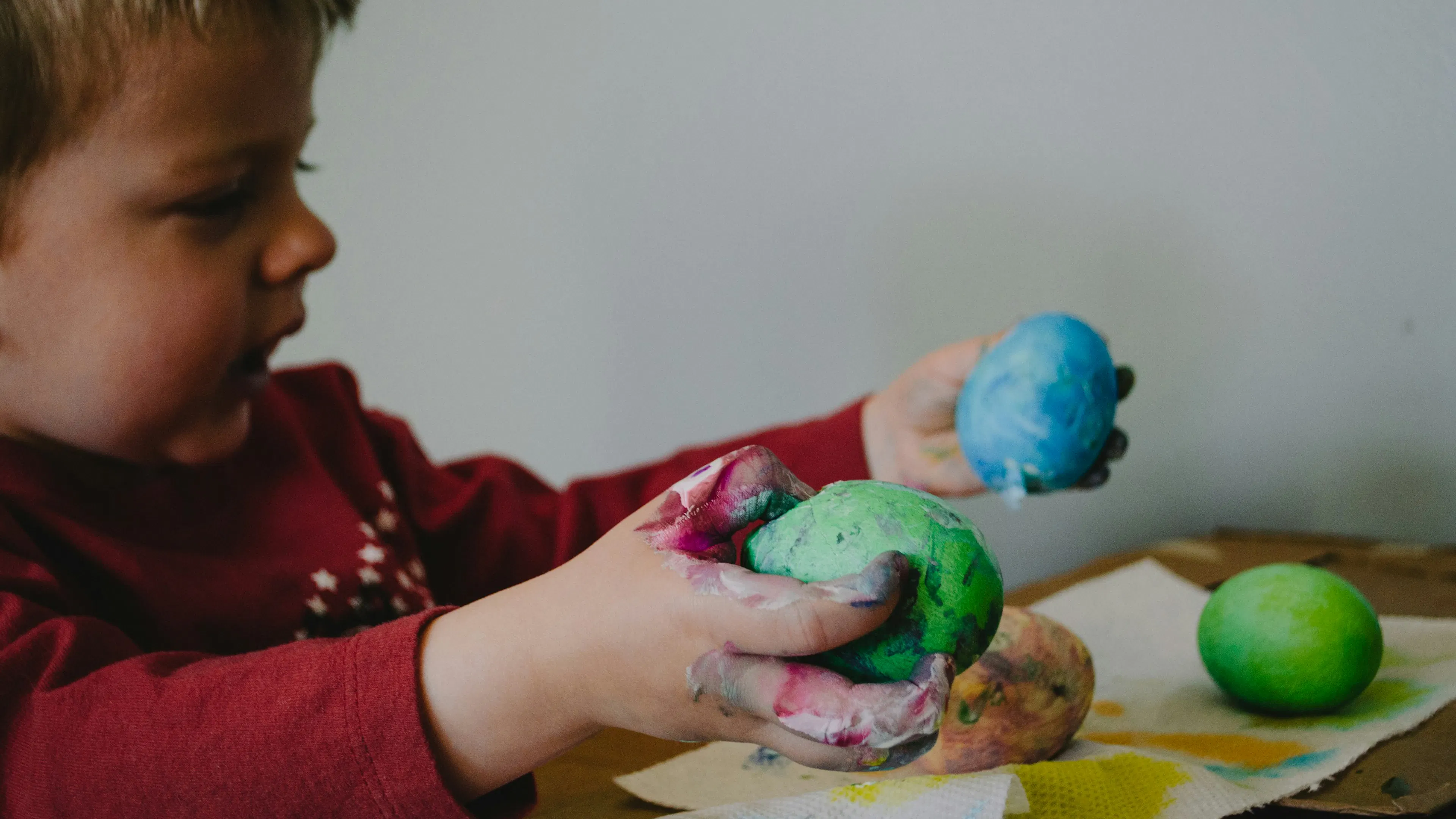 A boy in a red shirt playing with some painted eggs