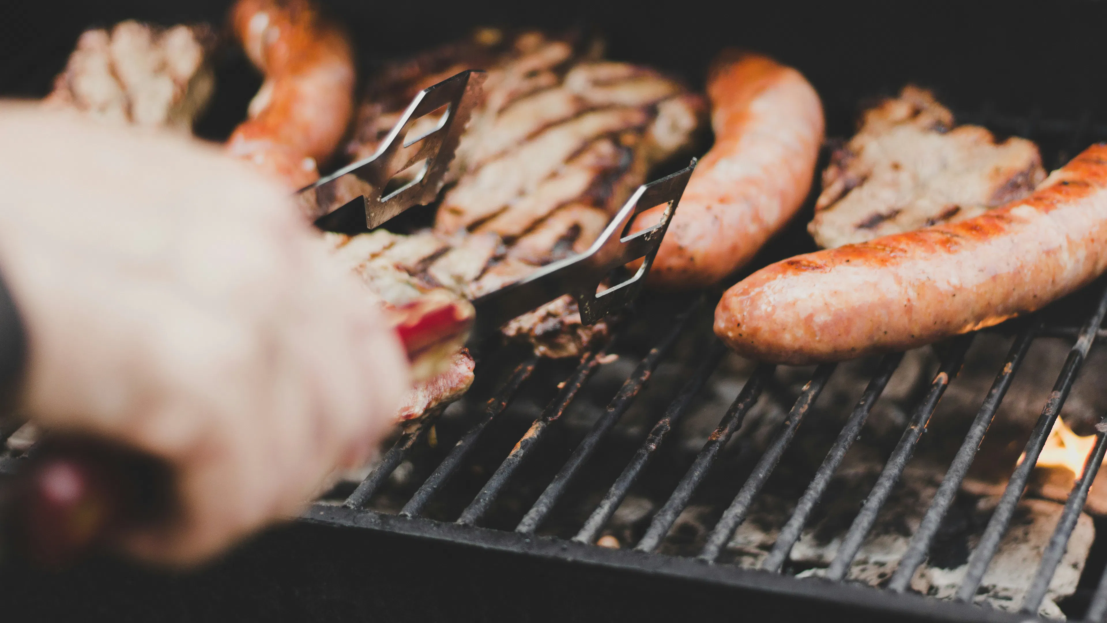 A person grilling meats on a grill using tongs