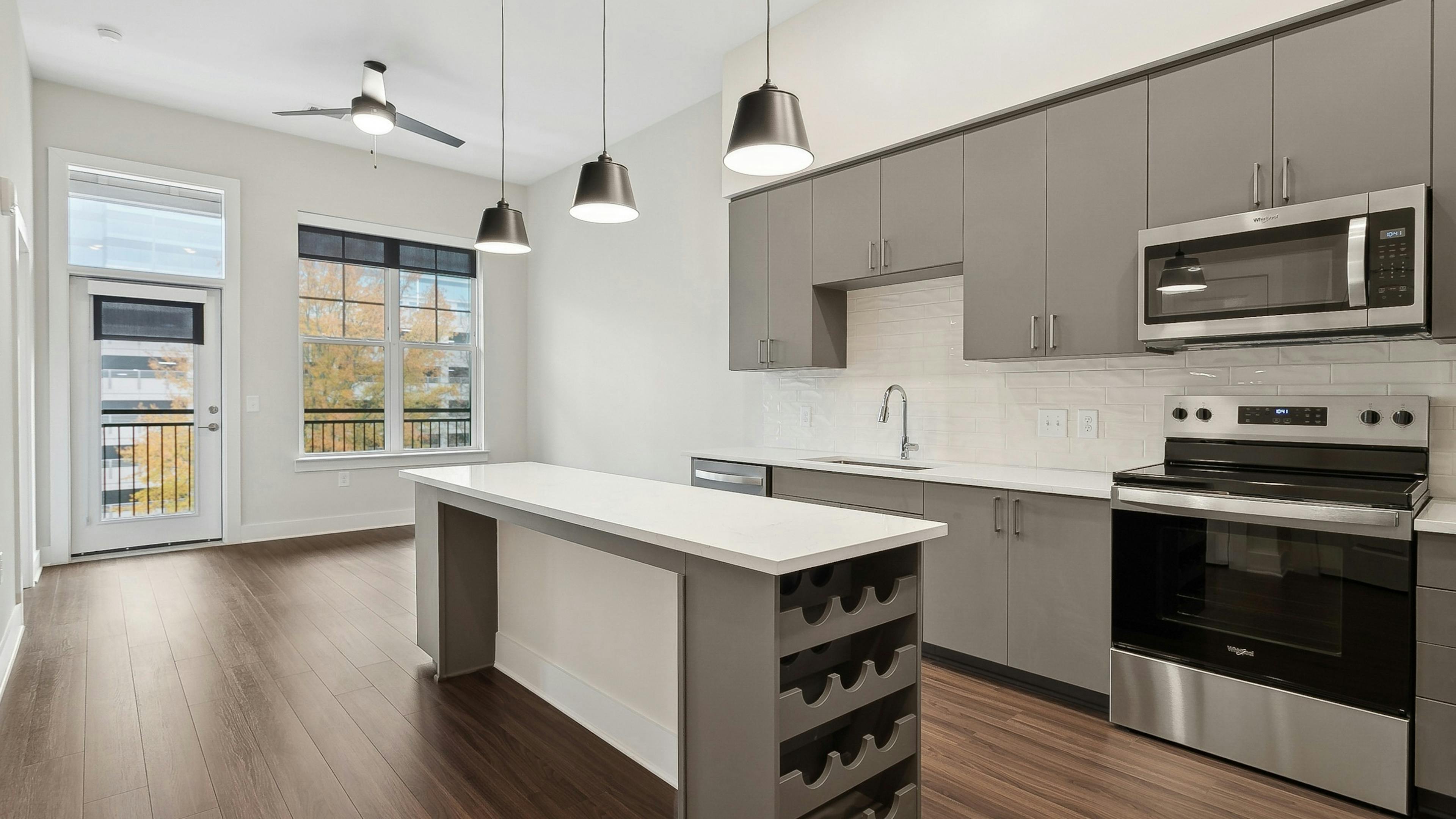 An interior view of am island kitchen at AMLI Brookhaven with a built in wine rack, gray cabinets, pendant lights and a ceiling fan