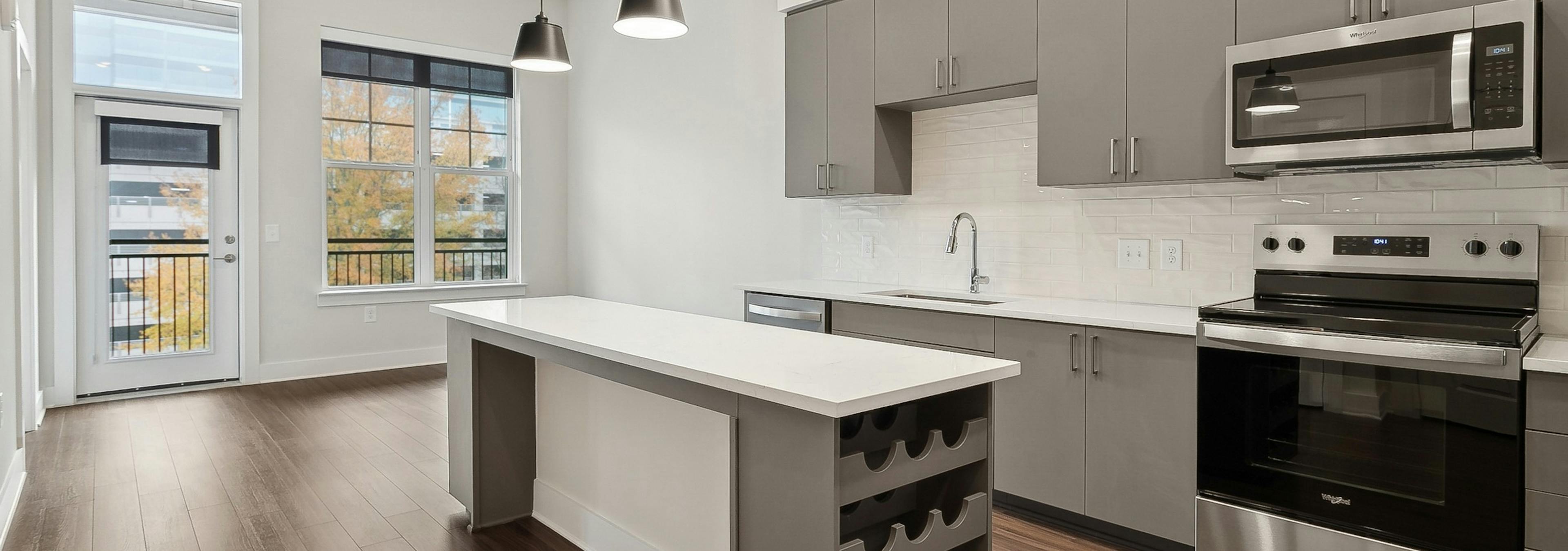 An interior view of am island kitchen at AMLI Brookhaven with a built in wine rack, gray cabinets, pendant lights and a ceiling fan