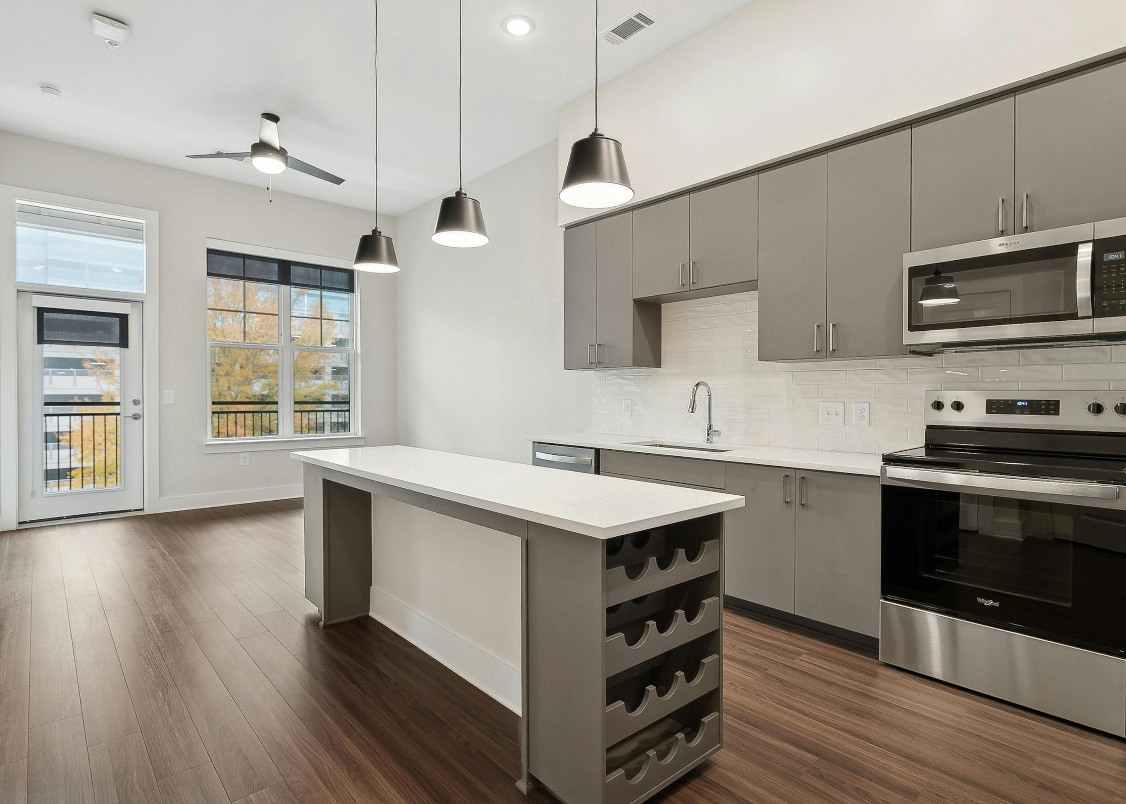 An interior view of am island kitchen at AMLI Brookhaven with a built in wine rack, gray cabinets, pendant lights and a ceiling fan