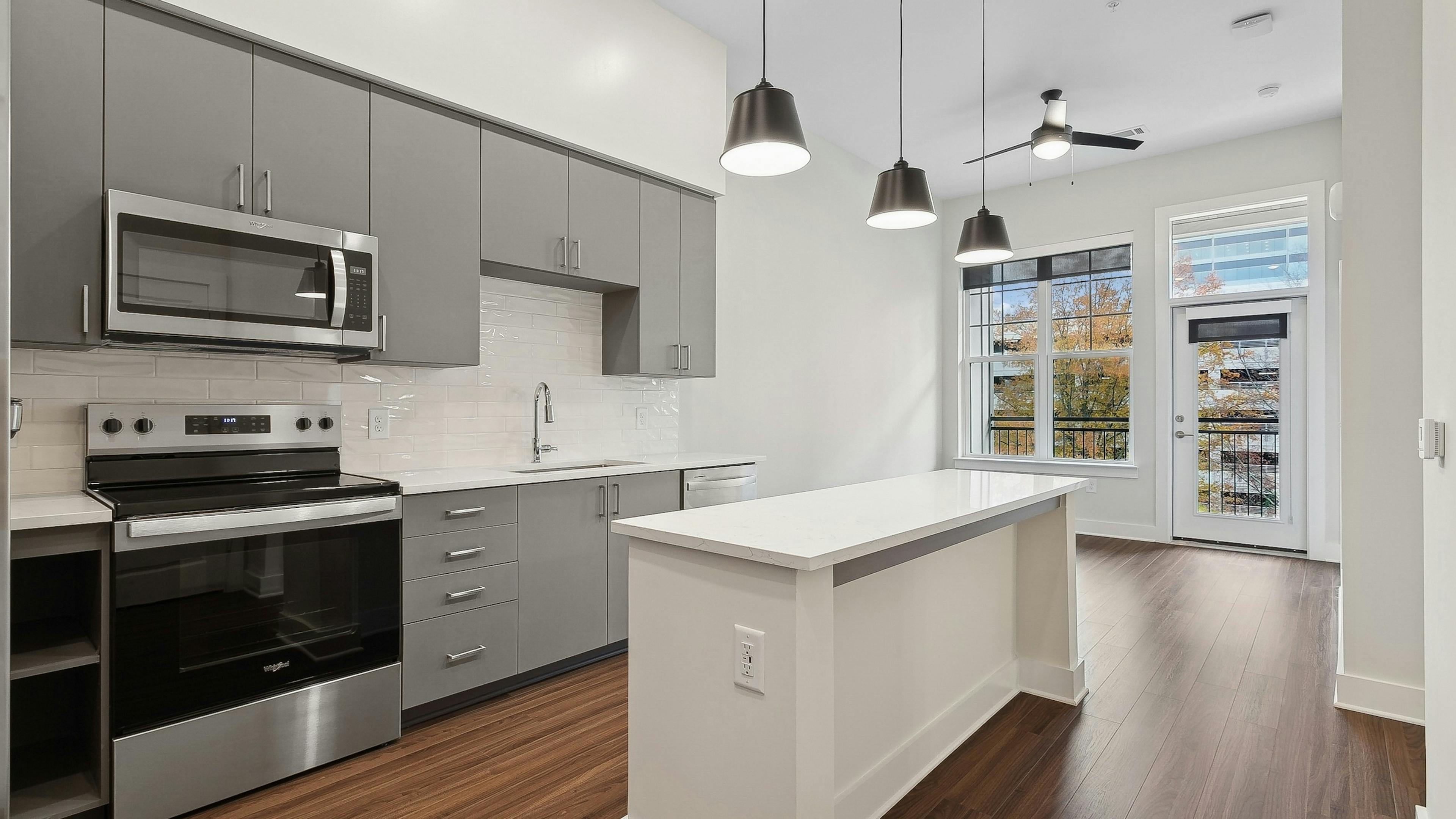 Kitchen at AMLI Brookhaven apartments with a white tile backsplash, gray caninets and windows with a view of trees and sky