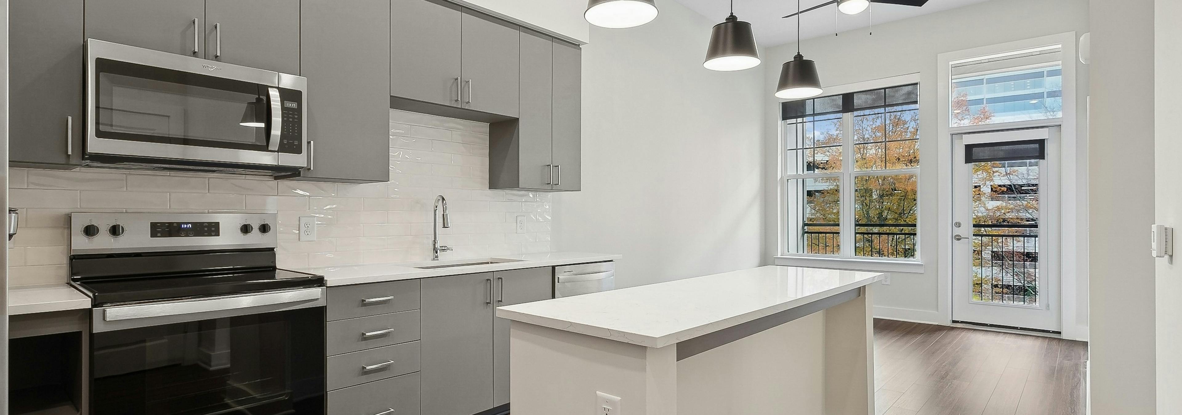 Kitchen at AMLI Brookhaven apartments with a white tile backsplash, gray caninets and windows with a view of trees and sky