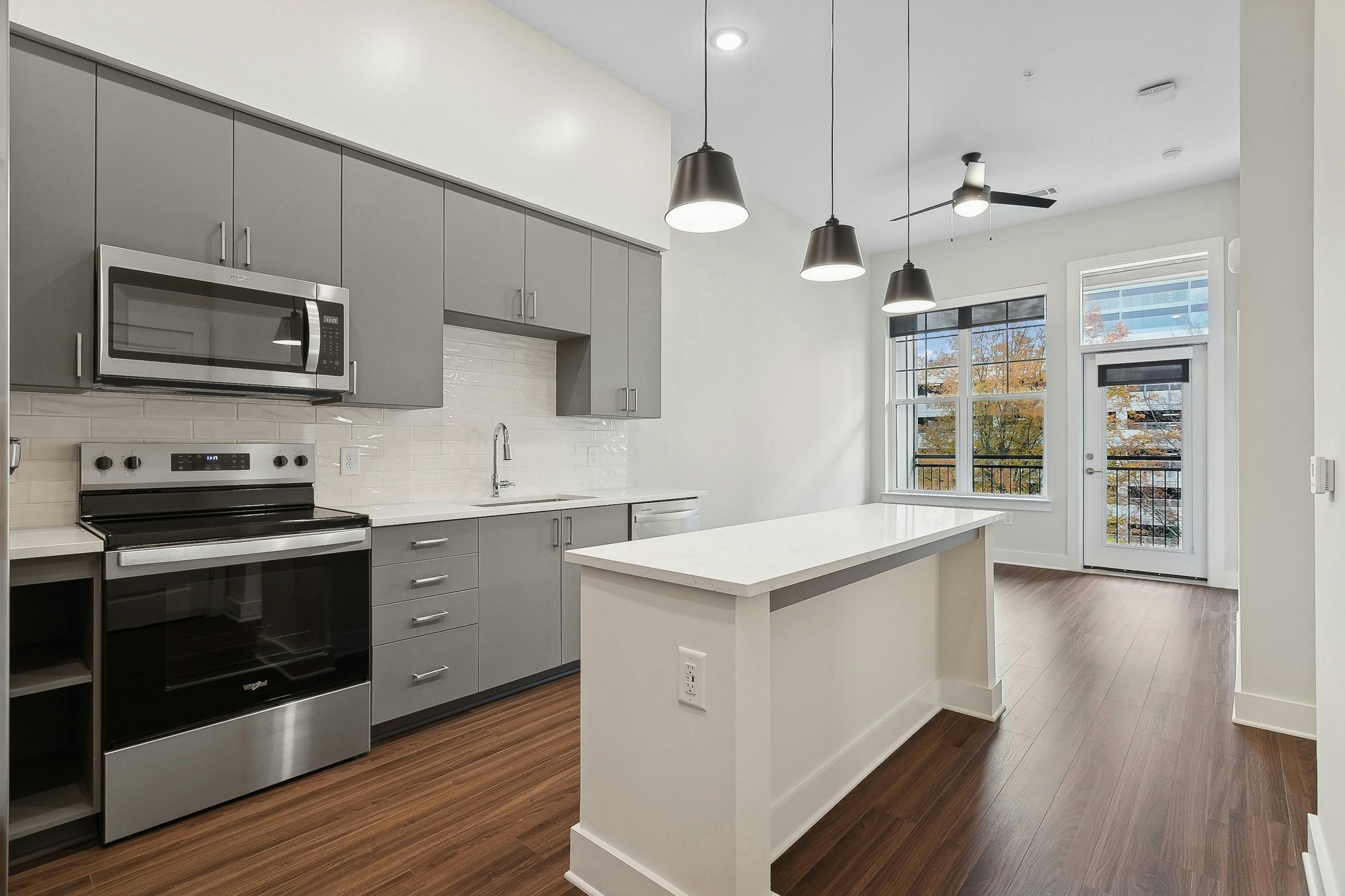 Kitchen at AMLI Brookhaven apartments with a white tile backsplash, gray caninets and windows with a view of trees and sky