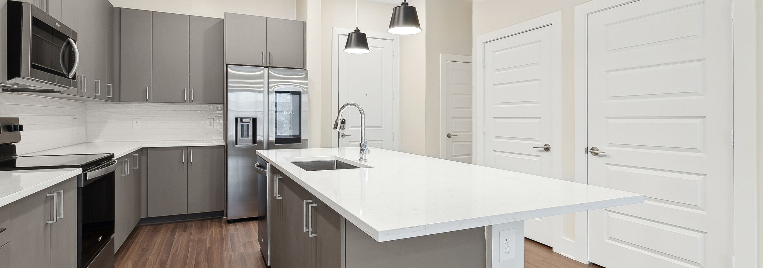 An AMLI Brookhaven apartment kitchen with white quartz countertops, wood flooring and a stainless steel smart refrigerator with touchscreen