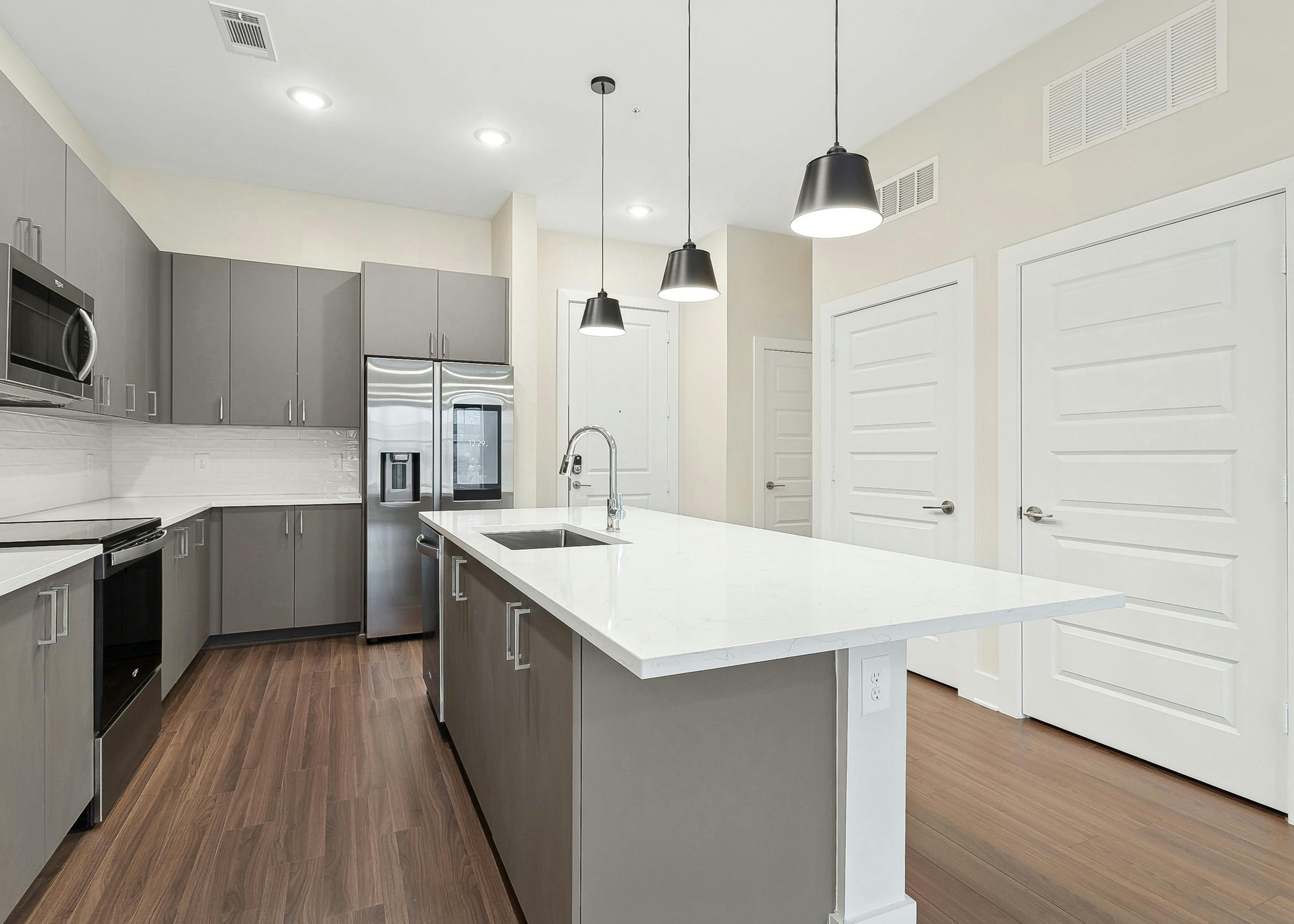 An AMLI Brookhaven apartment kitchen with white quartz countertops, wood flooring and a stainless steel smart refrigerator with touchscreen
