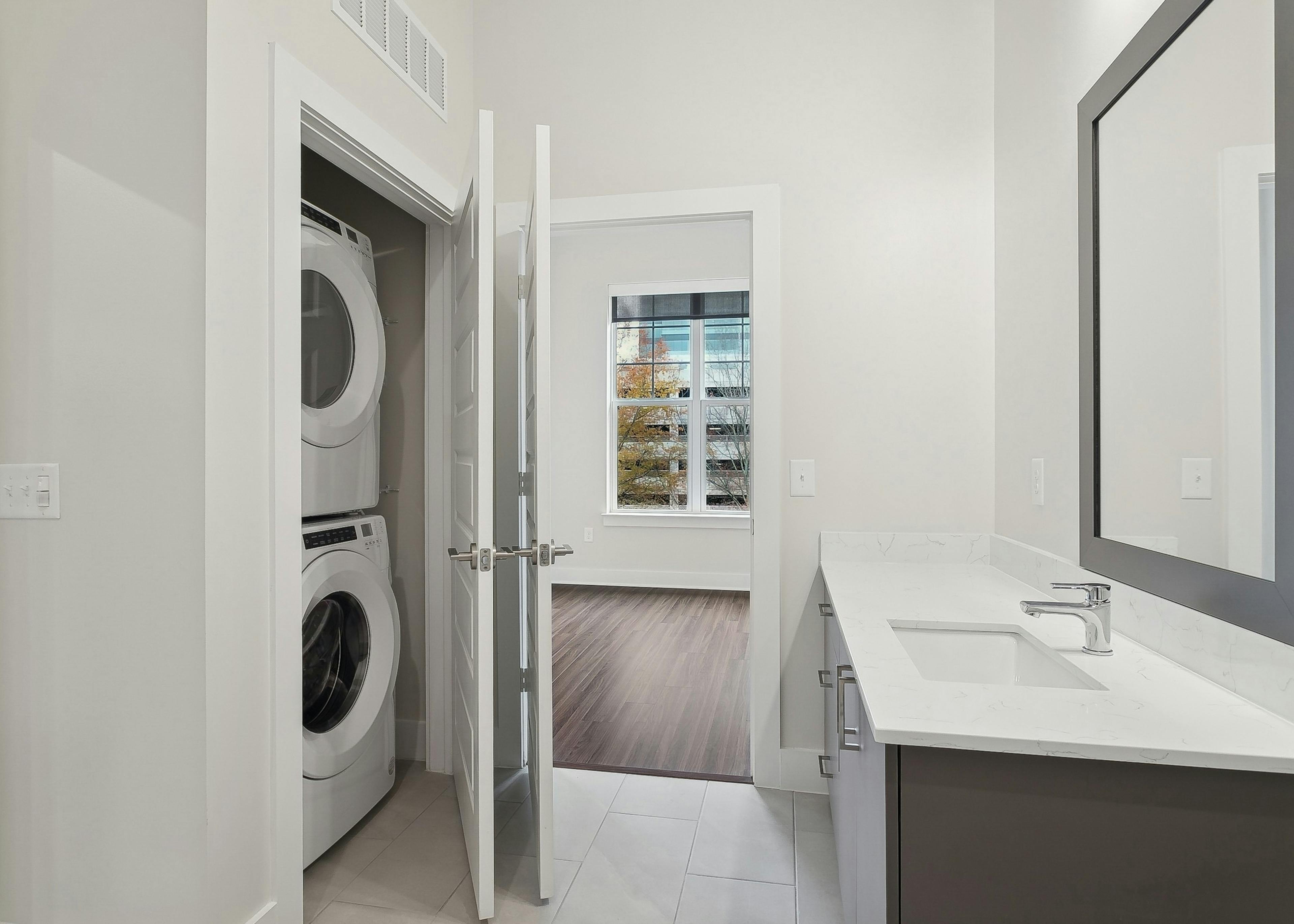 AMLI Brookhaven bathroom with a white countertop with mirror above across from a stacked washer and dryer with a view into a bedroom 