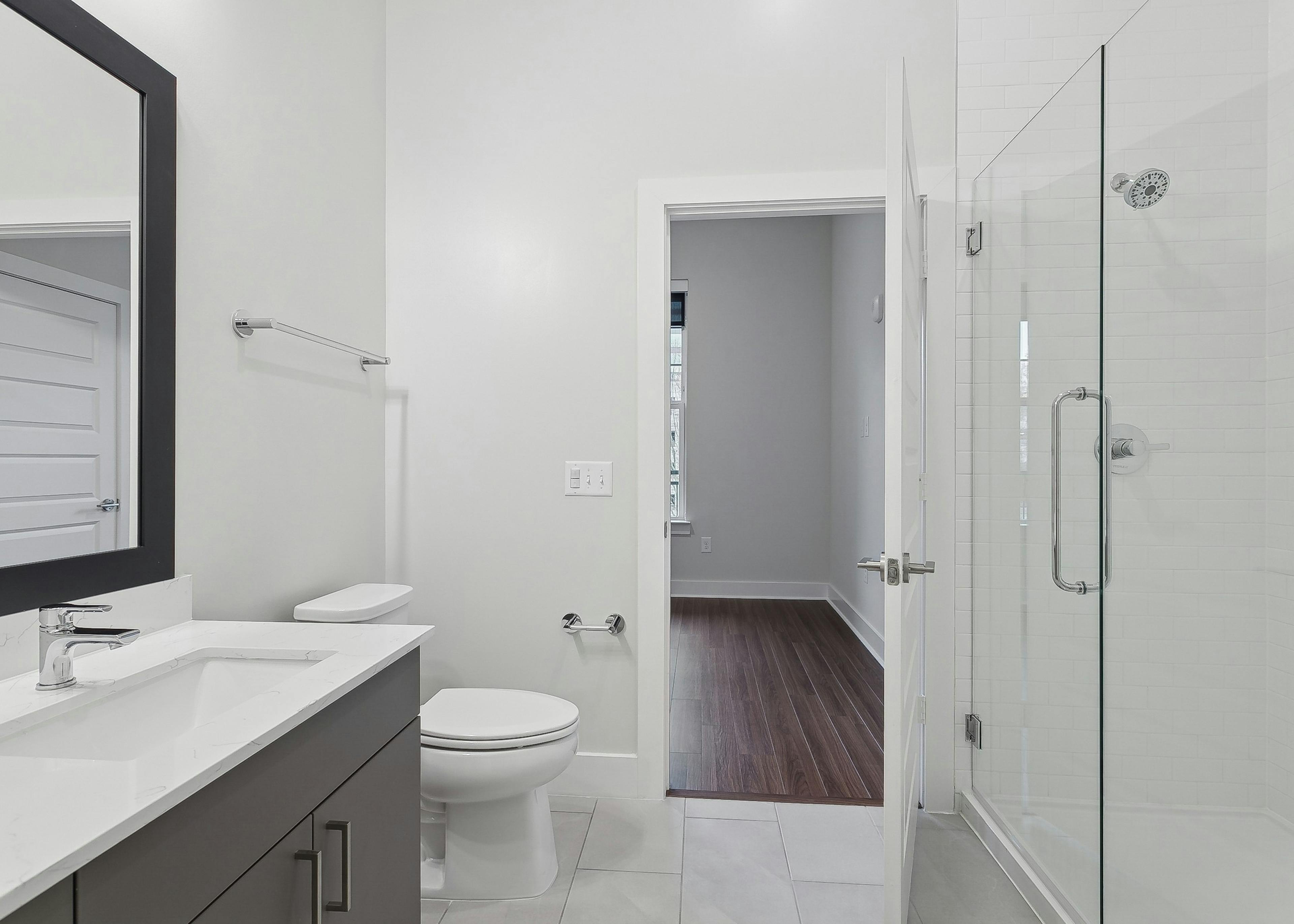 AMLI Brookhaven bathroom with a glass enclosed shower with floor to ceiling white tile and a view to an adjoining bedroom