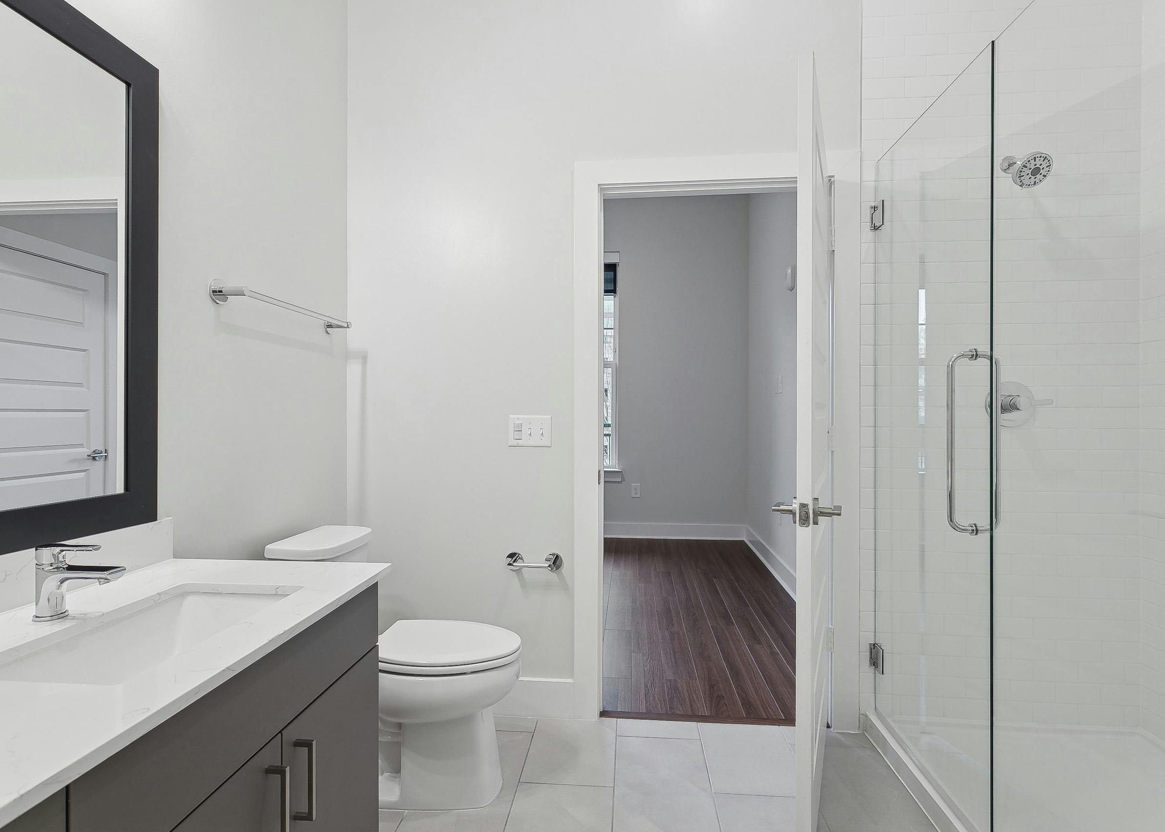 AMLI Brookhaven bathroom with a glass enclosed shower with floor to ceiling white tile and a view to an adjoining bedroom
