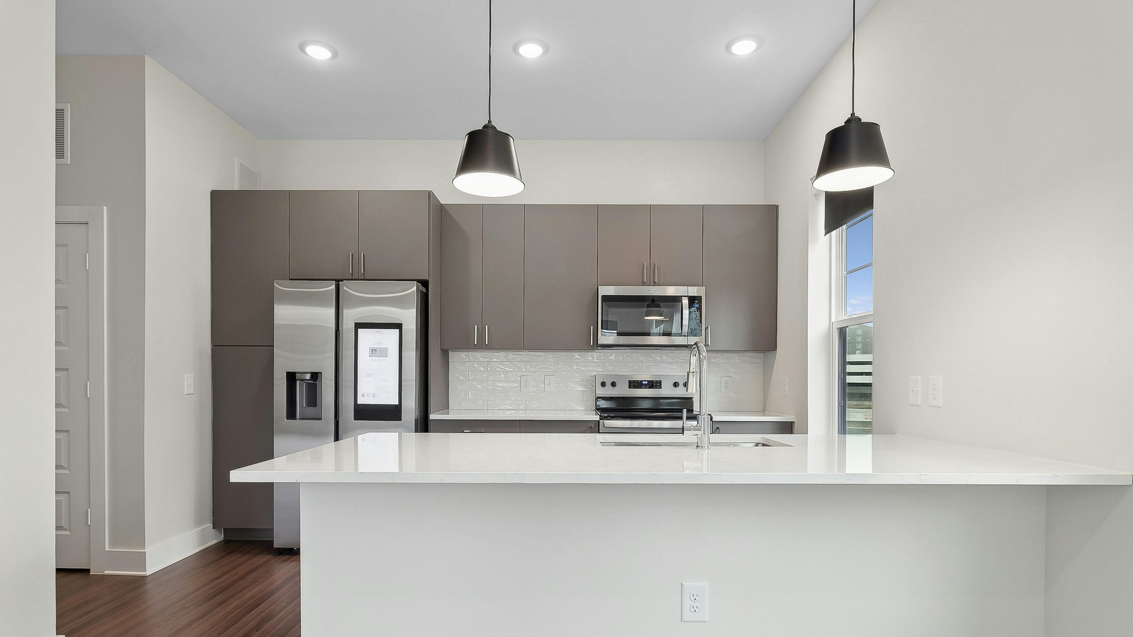 Interior view of a kitchen at AMLI Brookhaven with large white peninsula island, gray cabinets, a smart refrigerator and white backsplash