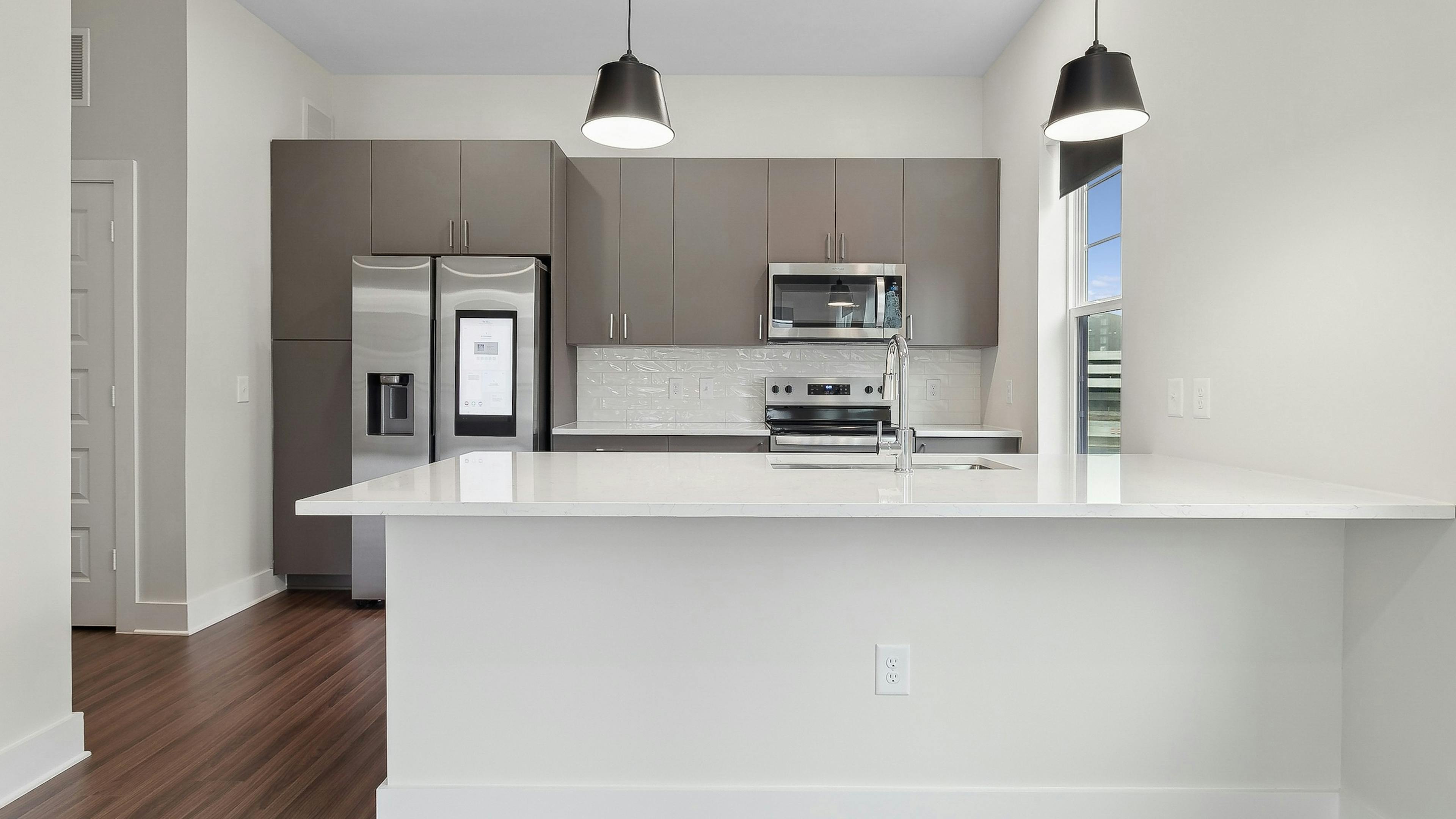 Interior view of a kitchen at AMLI Brookhaven with large white peninsula island, gray cabinets, a smart refrigerator and white backsplash