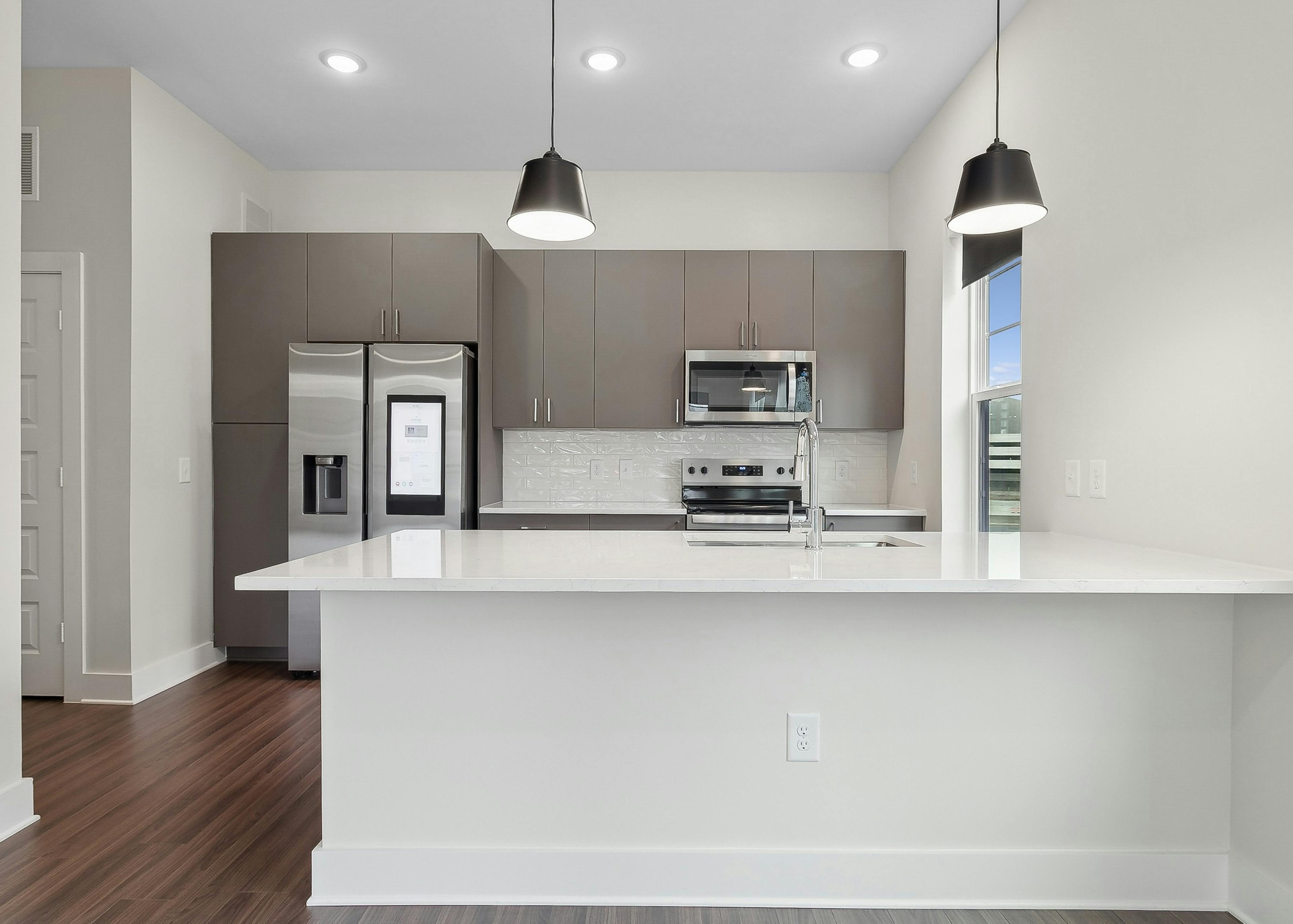 Interior view of a kitchen at AMLI Brookhaven with large white peninsula island, gray cabinets, a smart refrigerator and white backsplash