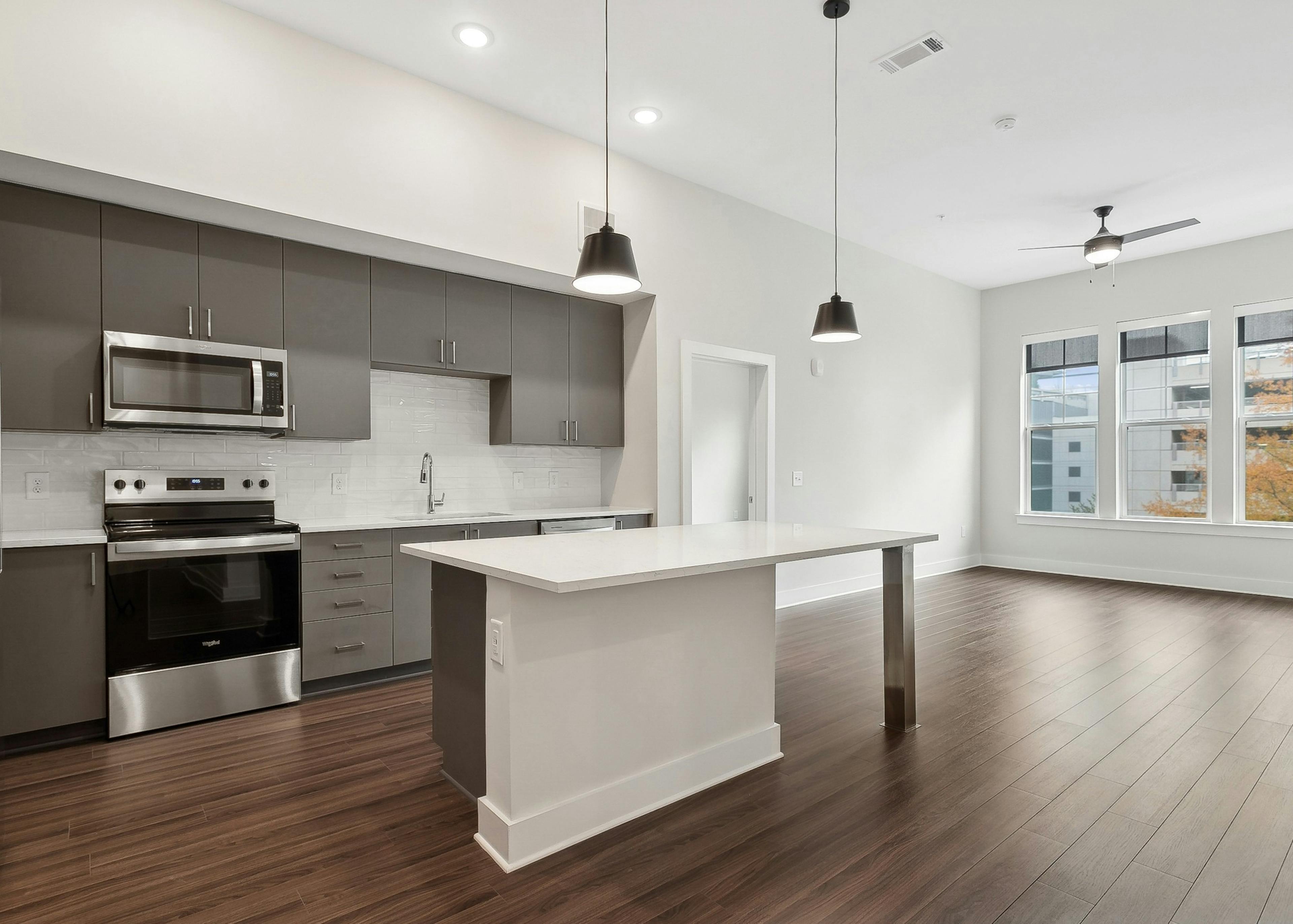 An island kitchen and living room at AMLI Brookhaven apartments with sleek gray cabinets, stainless steel appliances and large windows
