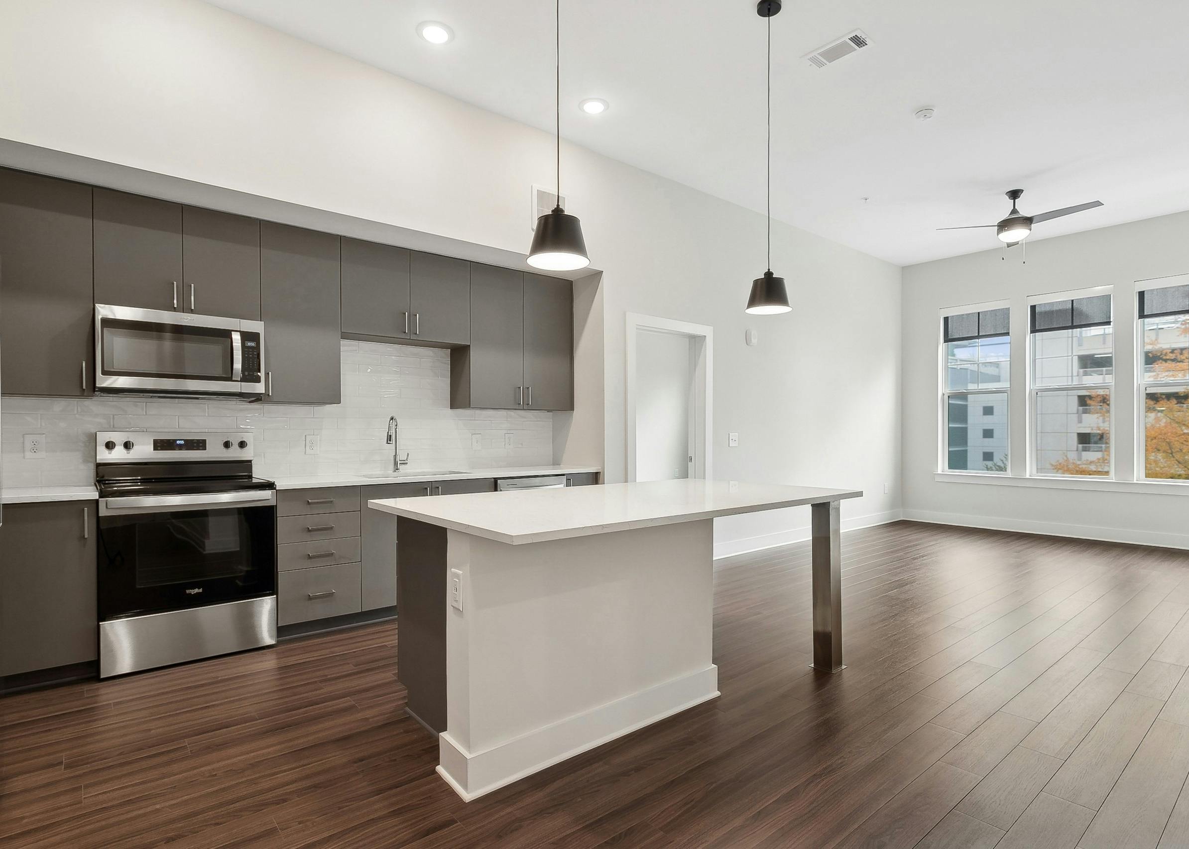 An island kitchen and living room at AMLI Brookhaven apartments with sleek gray cabinets, stainless steel appliances and large windows