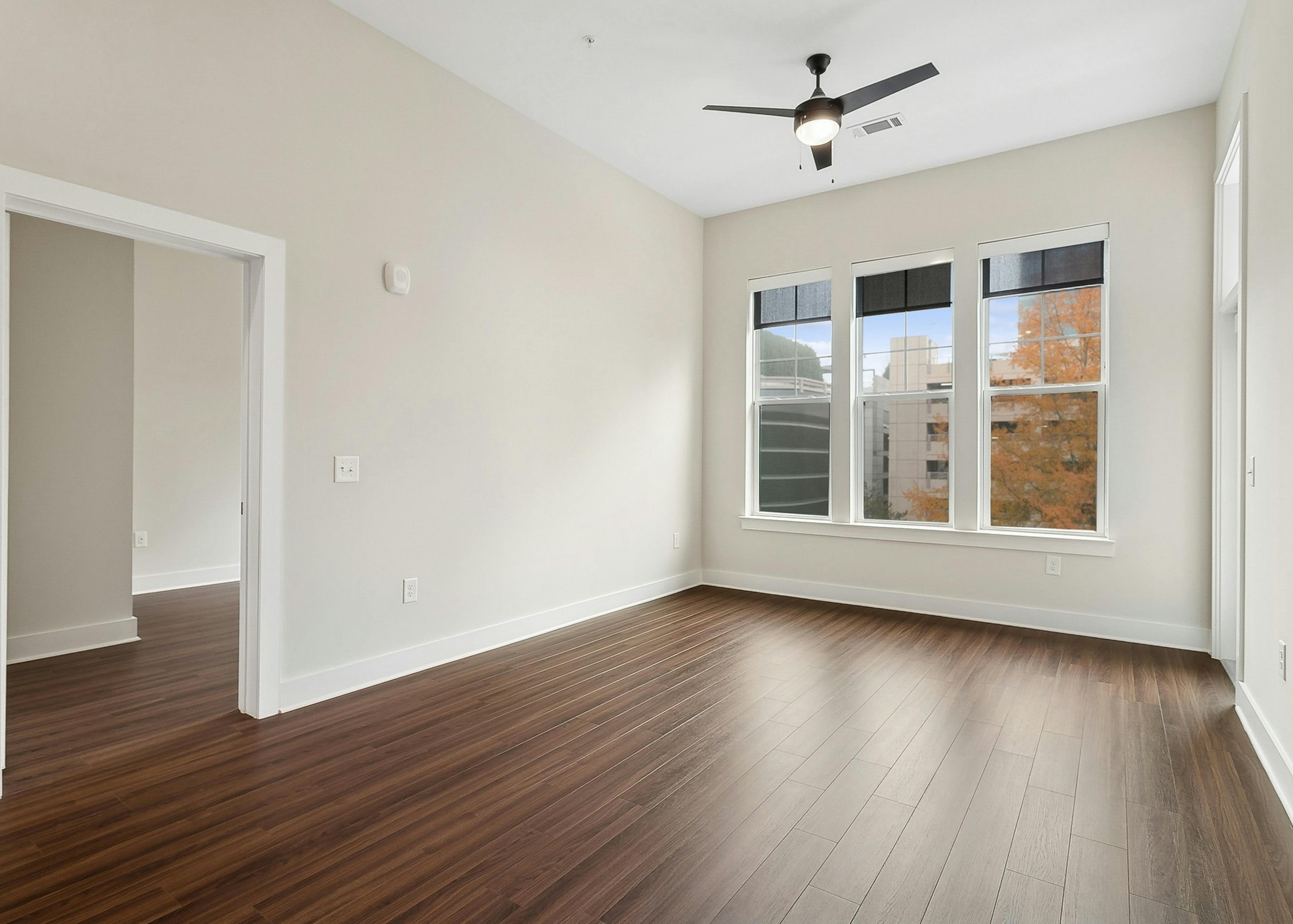 AMLI Brookhaven apartment living room with a view into a bedroom and 3 windows with solar shades and wood finish floors