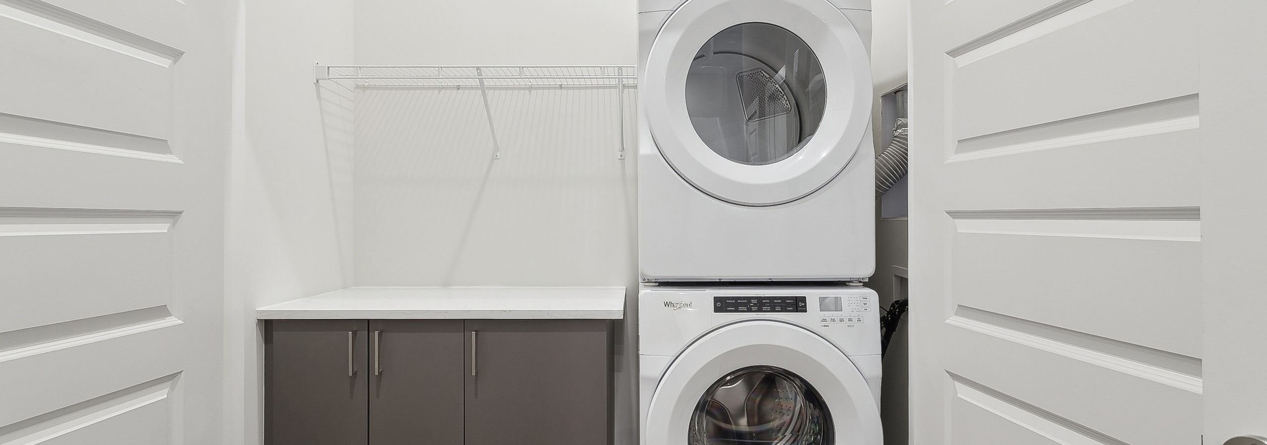 AMLI Brookhaven Laundry closet with full size stackable white washer and dryer beside a gray cabinet with shelf above it