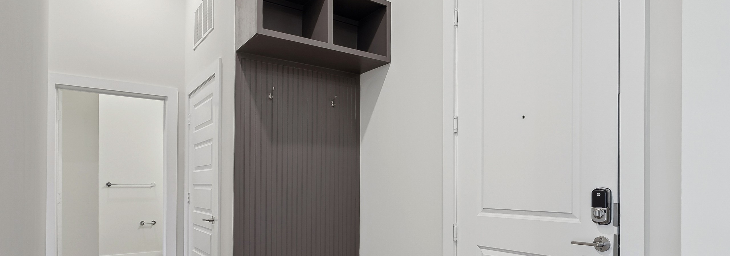 Mudroom area with gray wall with coat hooks and cubbies above adjacent to the front door at AMLI Brookhaven apartments