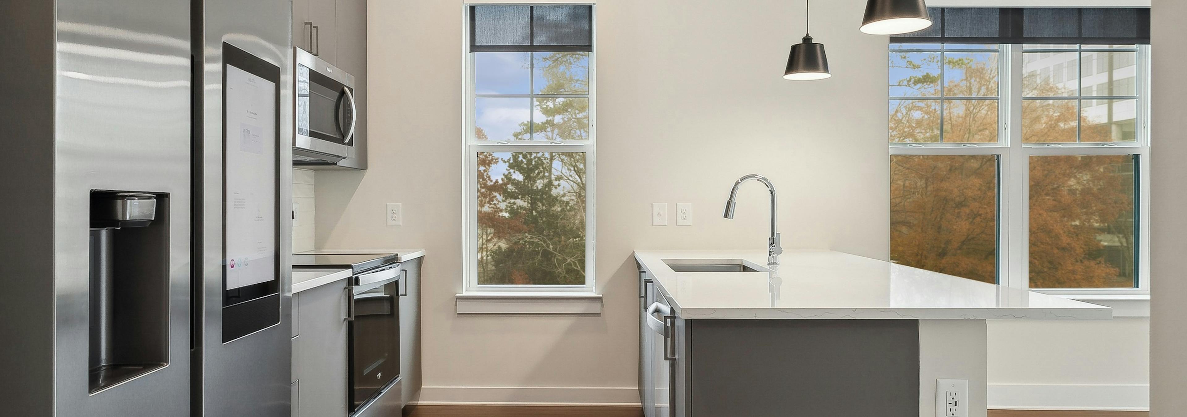 Interior view of a kitchen at AMLI Brookhaven with large white peninsula island, stainless steel appliances and 2 windows
