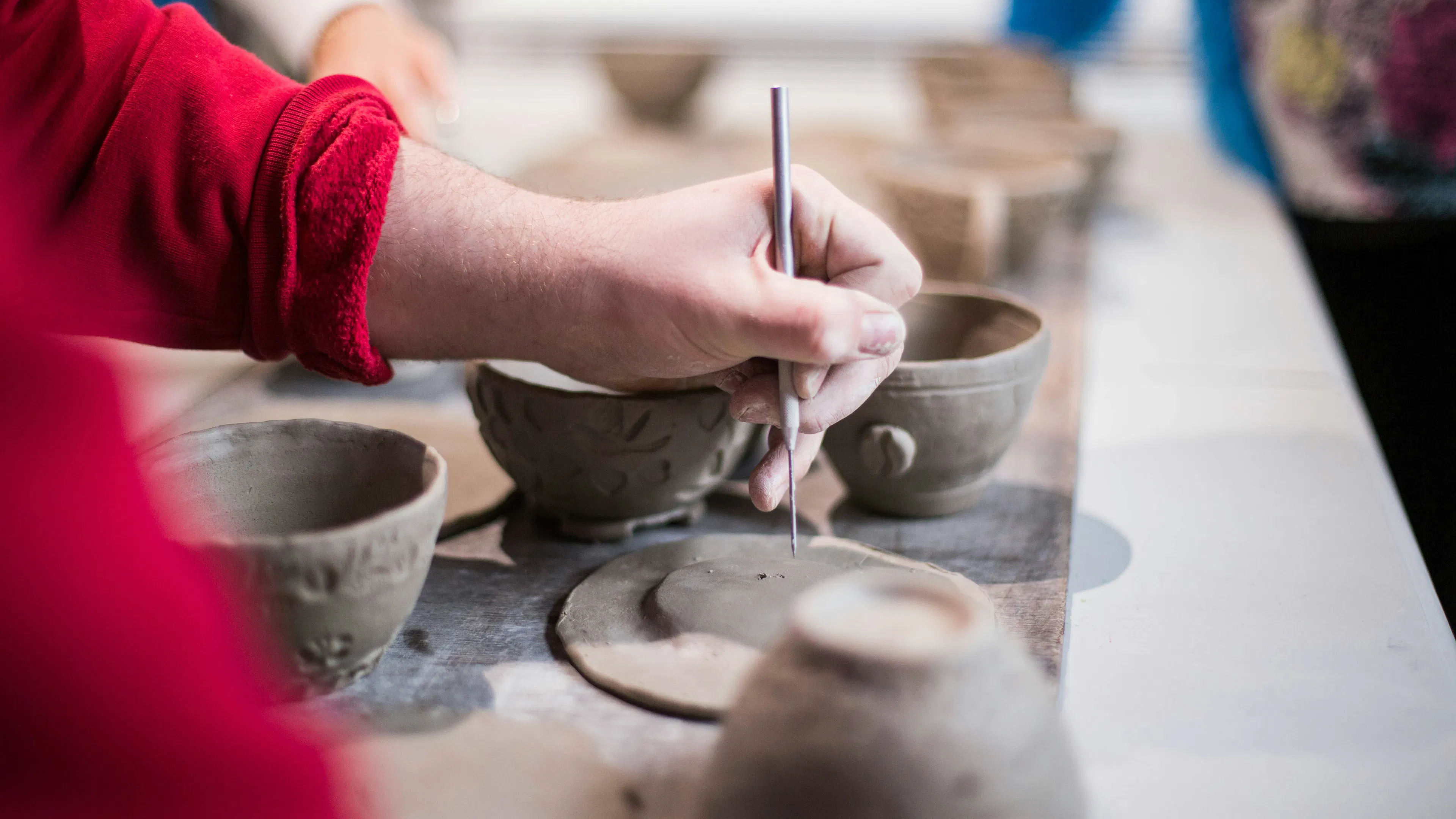 A person's hands adding detail to unfinished pottery pieces