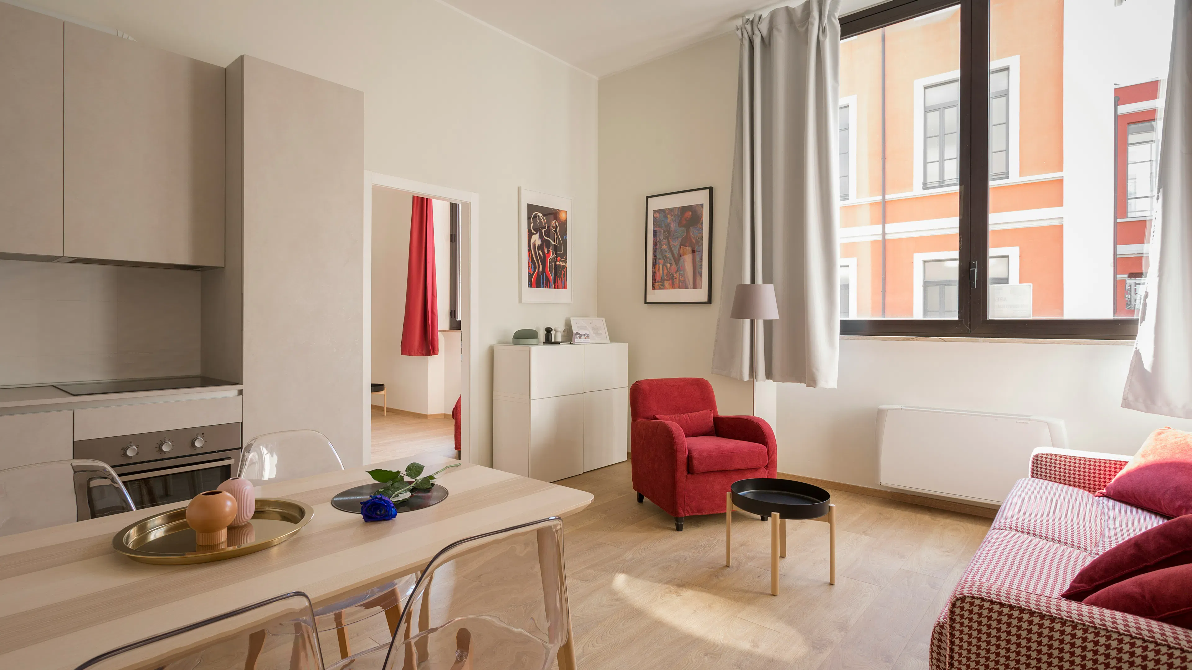 A bright and sunny apartment with a red armchair and red accents on the surrounding beige furniture
