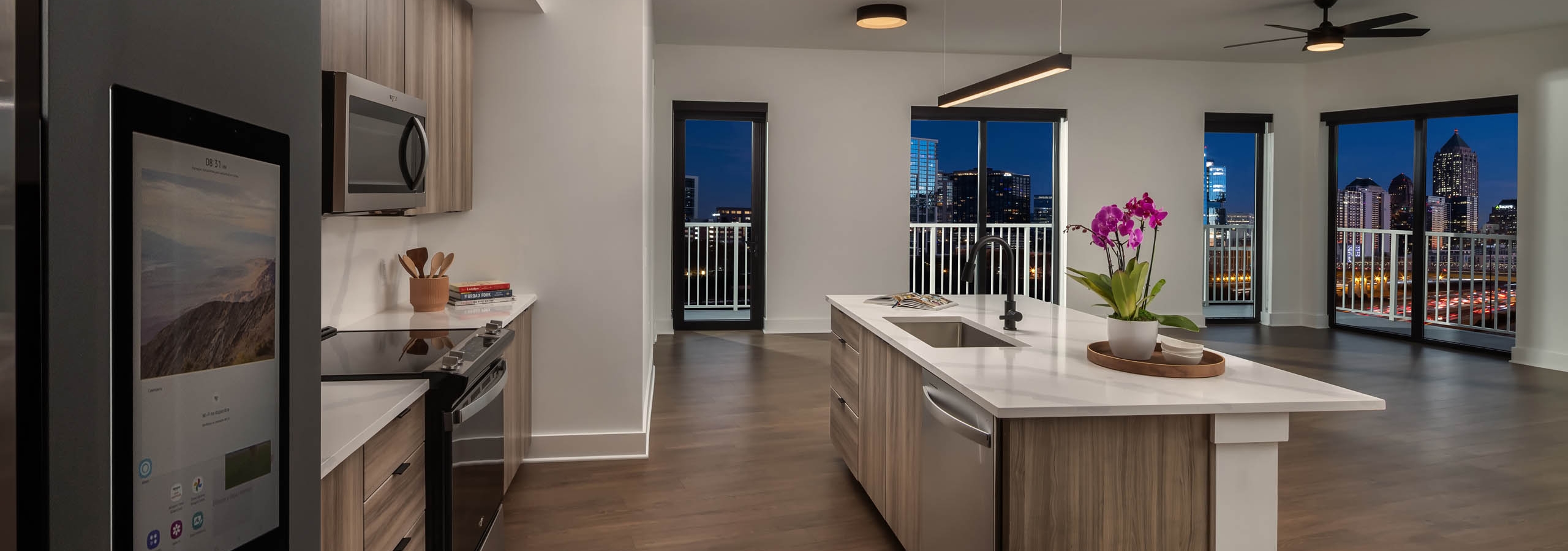 Night view of island kitchen and living area at AMLI Atlantic Station with stainless steel appliances wood cabinets and white countertops
